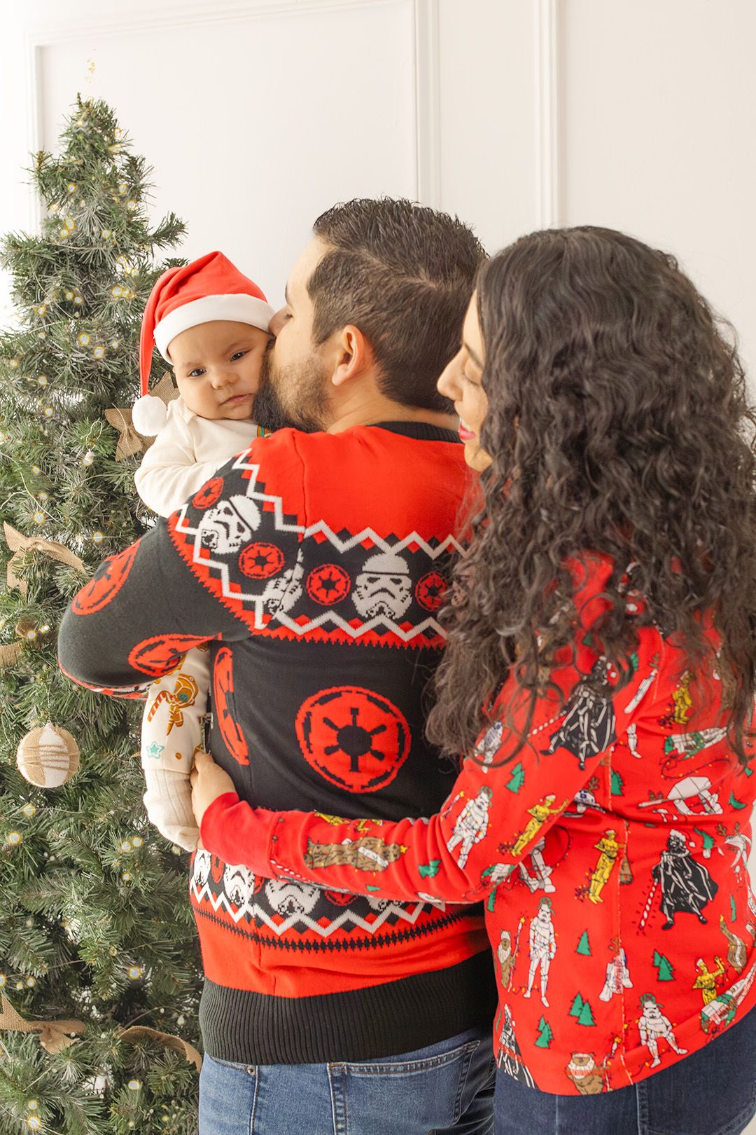Two people wearing festive Star Wars themed Christmas sweaters stand in front of a decorated tree.