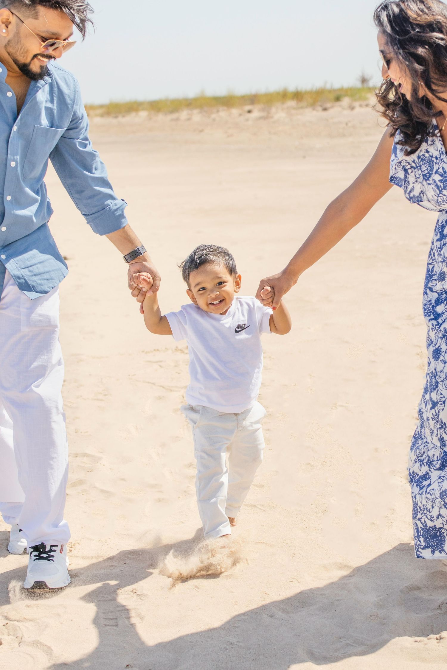 Family enjoys a sunny day at the beach, walking hand in hand together on the sand.