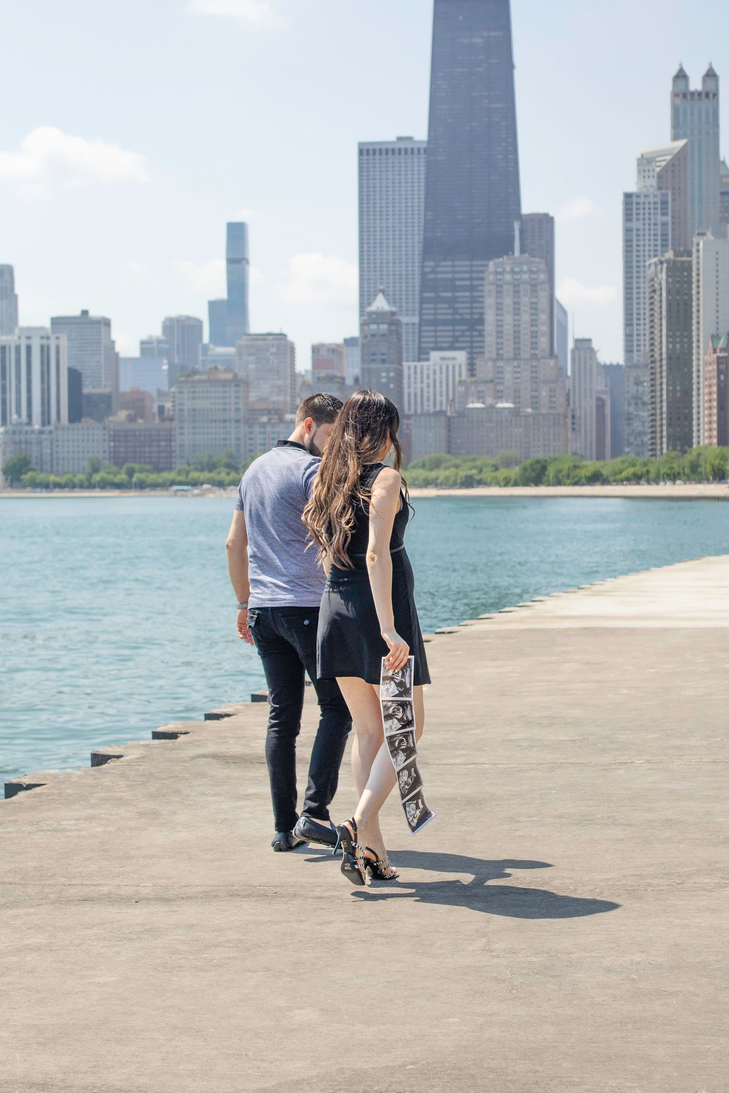 A couple strolls along Lake Michigan pier with Chicago's iconic skyline and John Hancock building in the background.