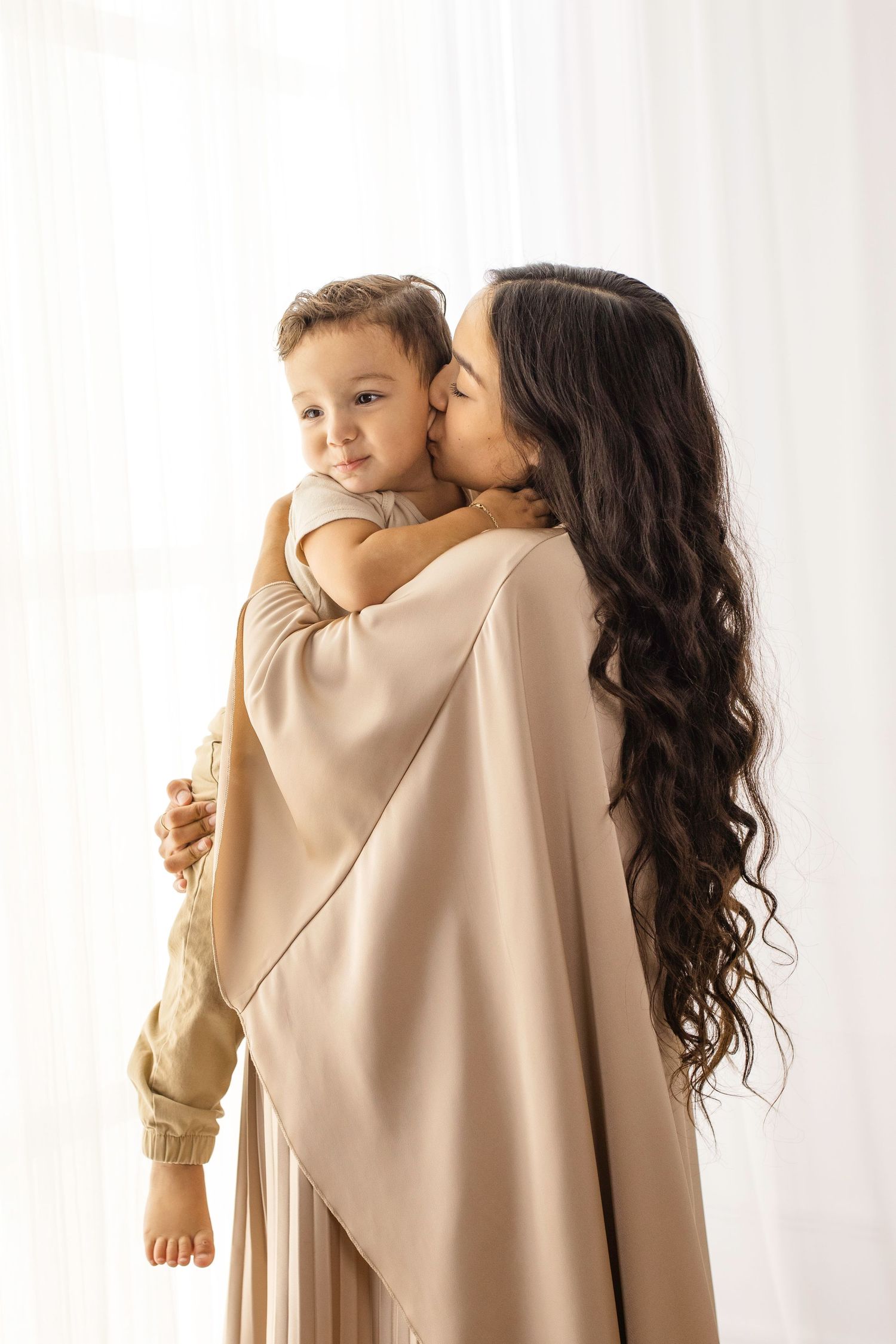 Parent and child in matching beige outfits share tender moments in minimalist studio portraits.
