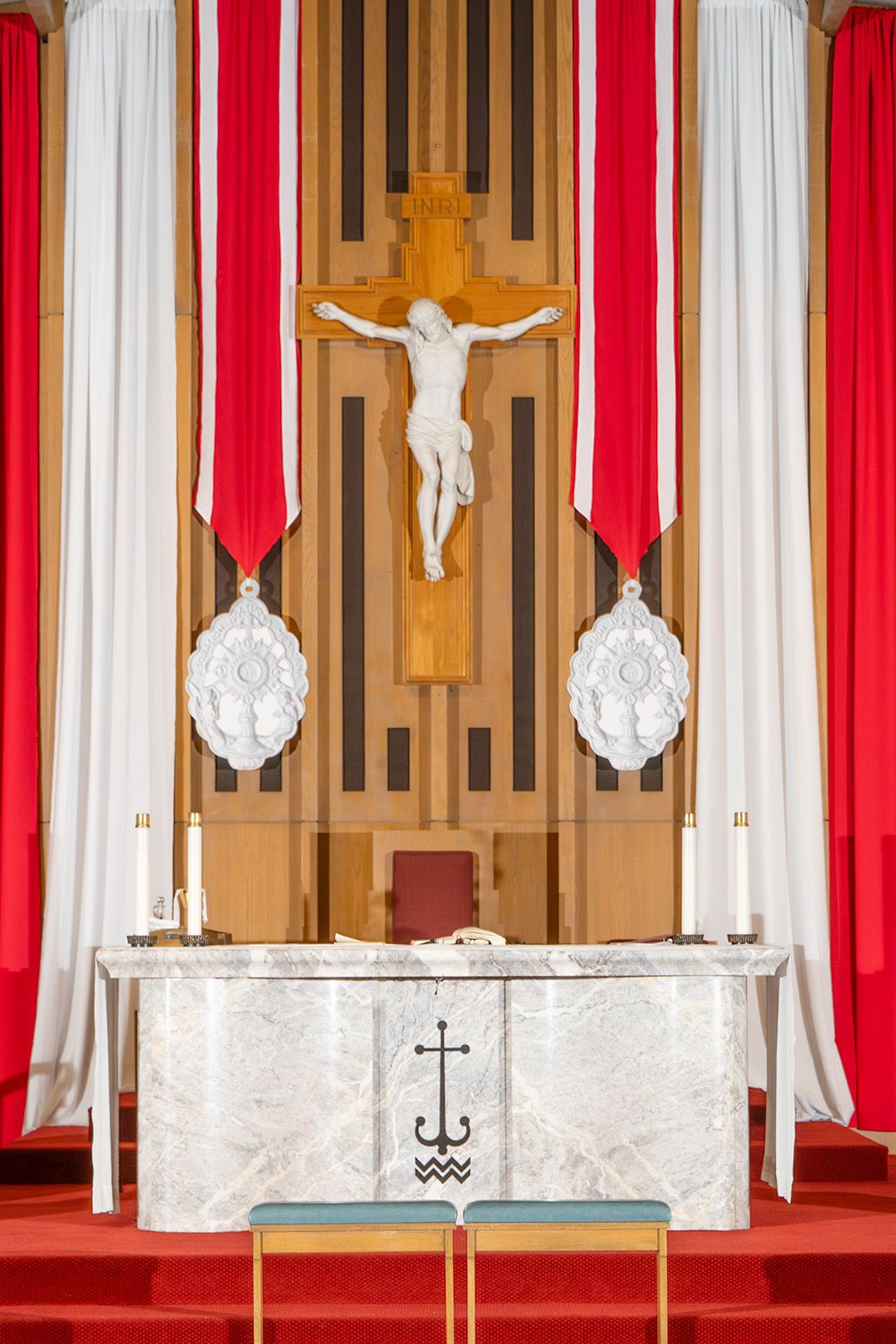 Church altar with crucifix, white marble table, red drapes, and candles in a Catholic chapel.