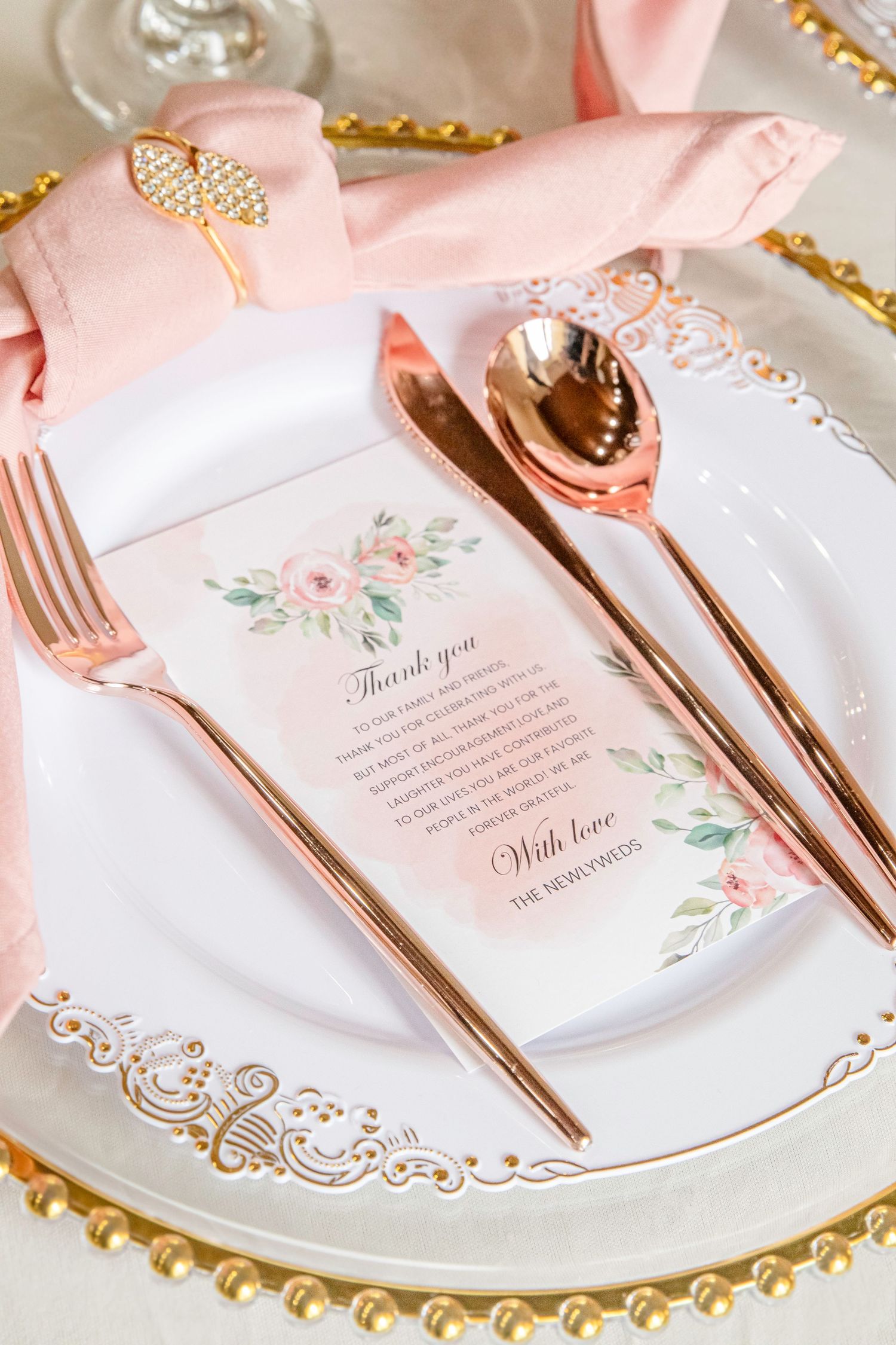 Elegant pink and gold wedding place setting with floral menu cards, rose gold utensils, and delicate lace details.