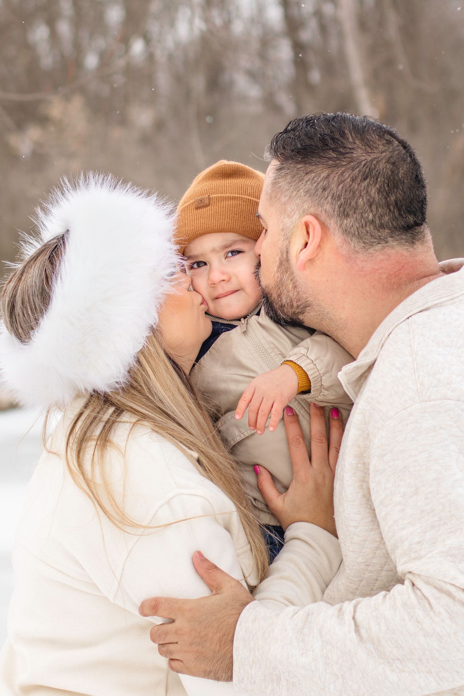 Intimate family moment in winter snow with small child in brown beanie.