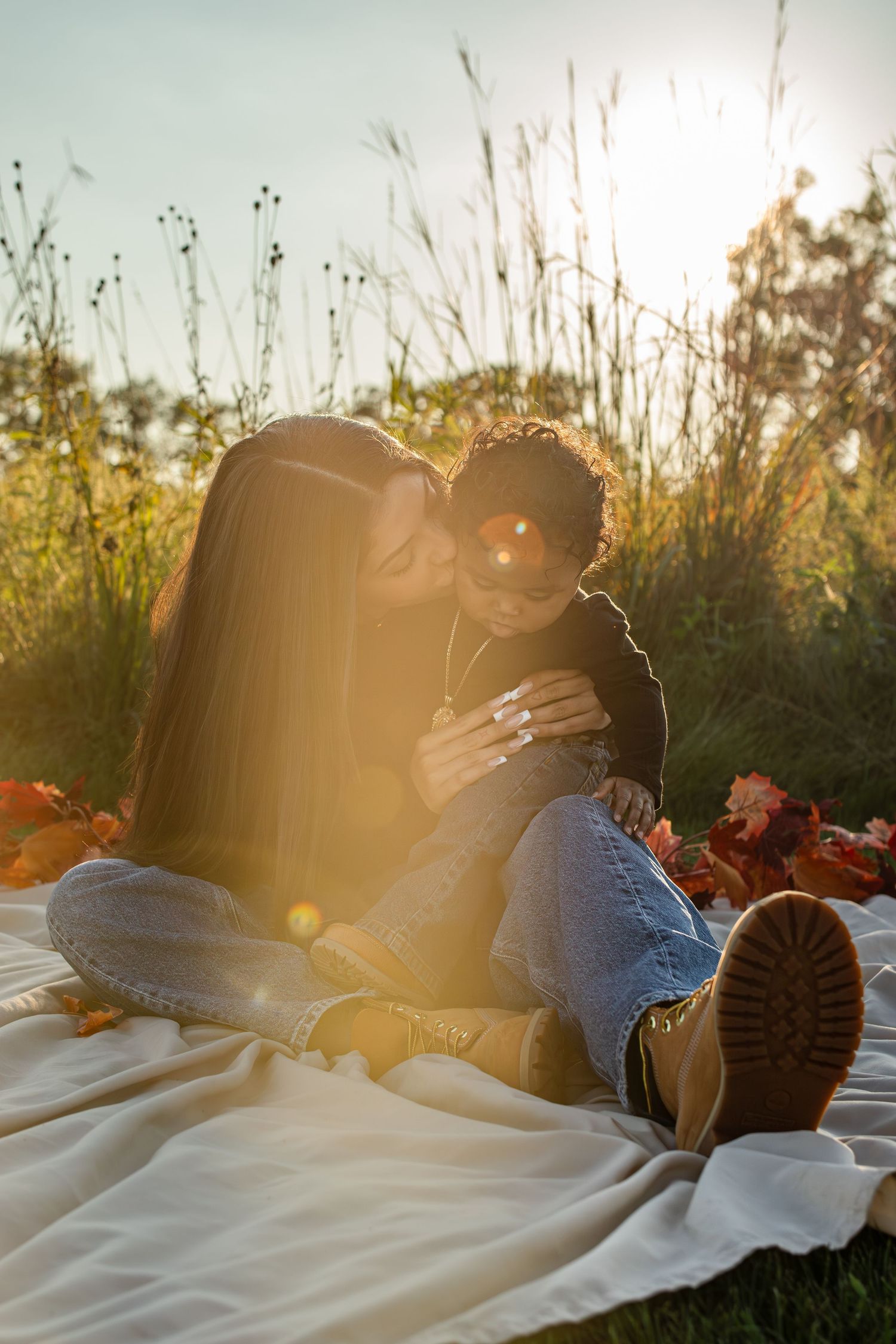 A couple lying in white sheets on grass at sunset with golden sunlight streaming through tall grass.