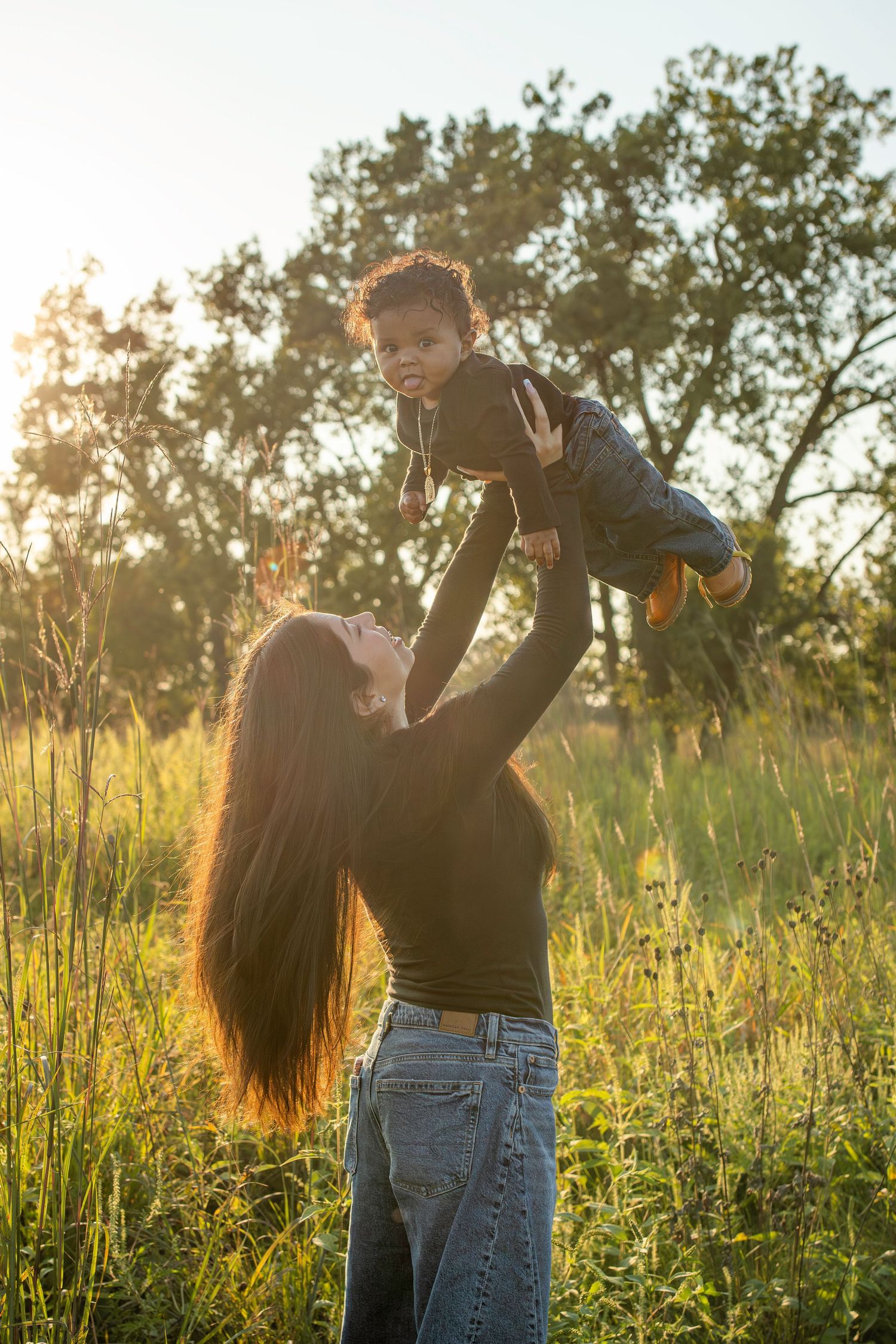 Romantic couple sharing intimate moments at golden hour in a sunlit meadow with tall grass and trees in background.