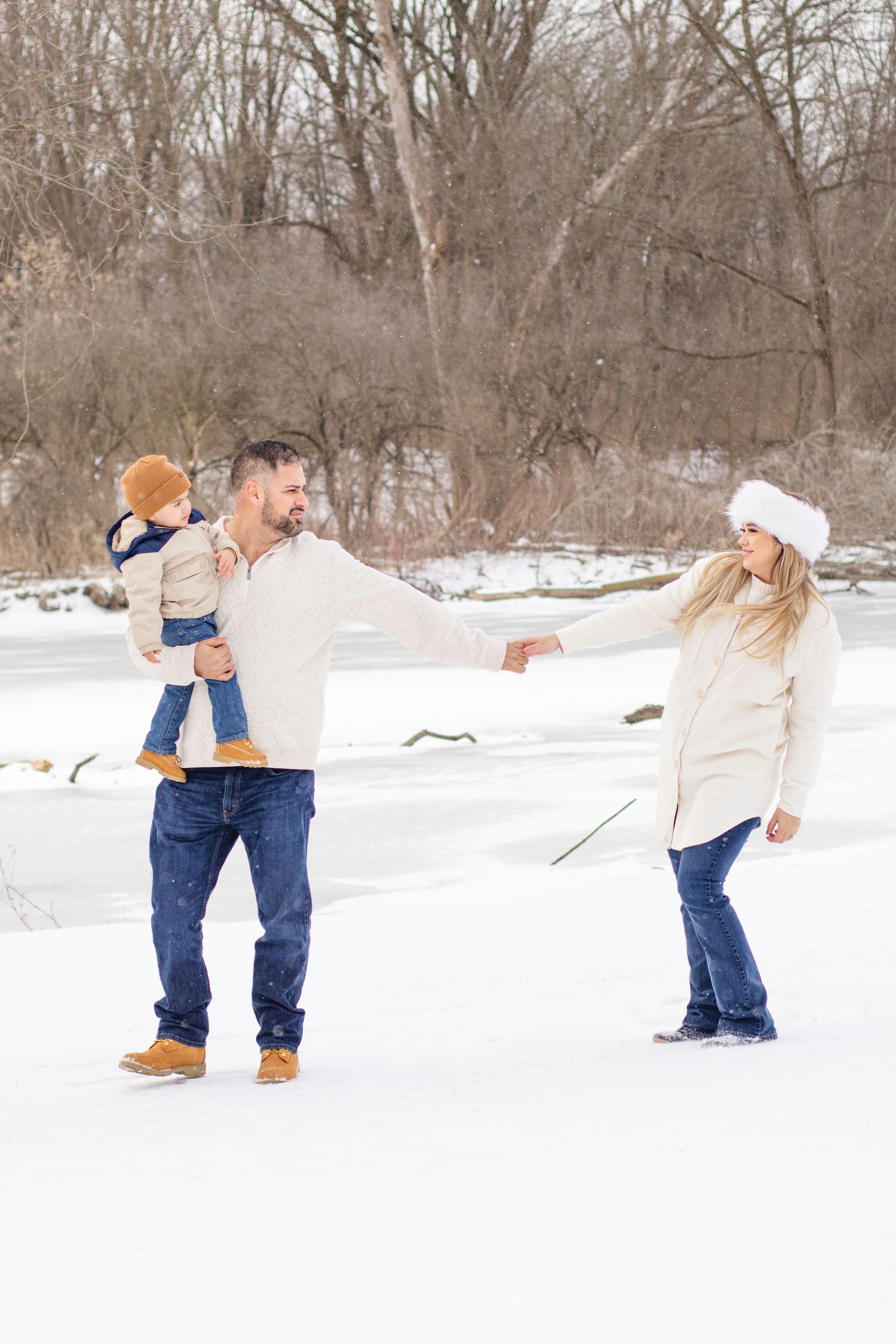 Playful winter family moment in snow with cream sweaters.