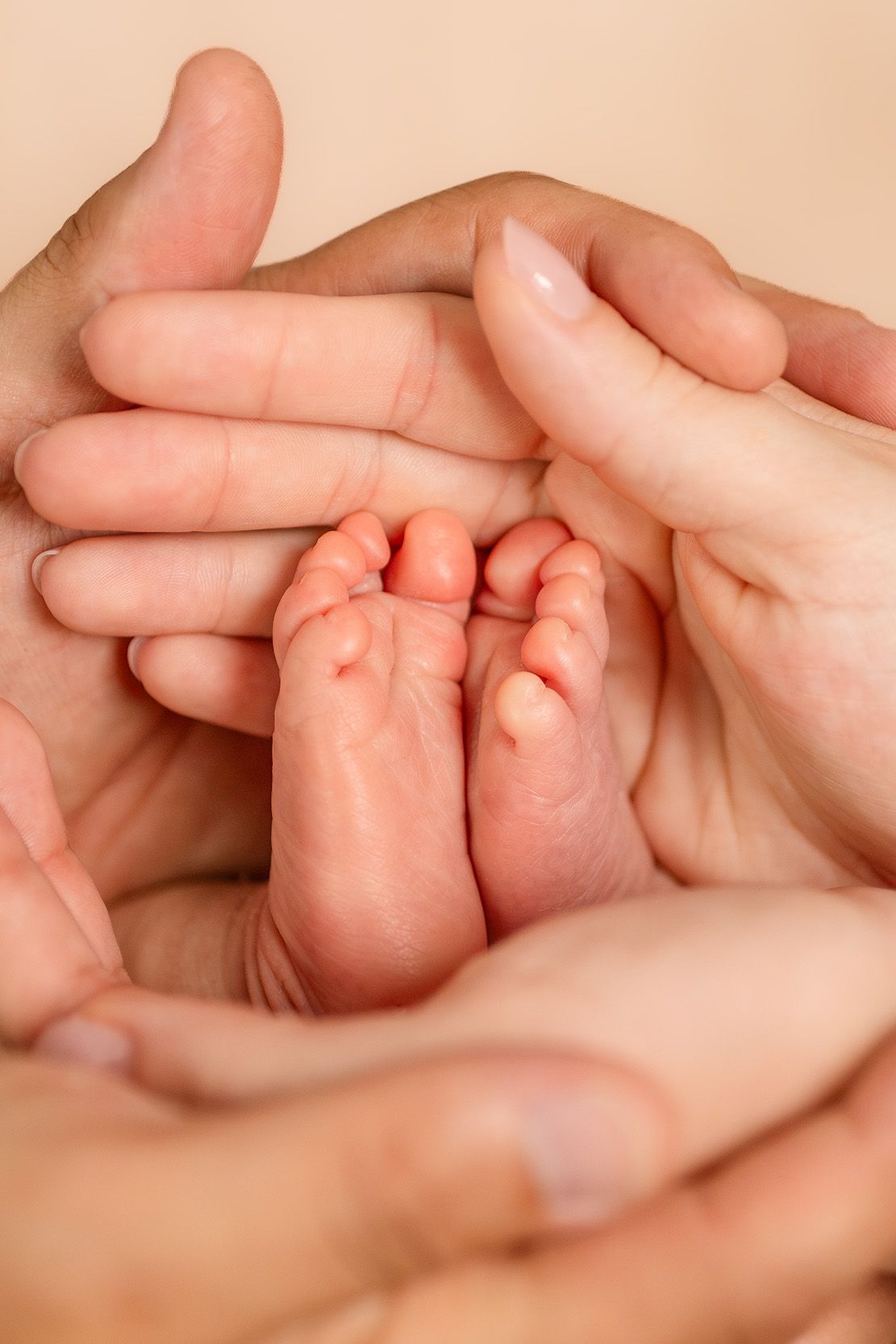 Adult hands gently cradling tiny newborn baby feet, symbolizing parental love and protection.