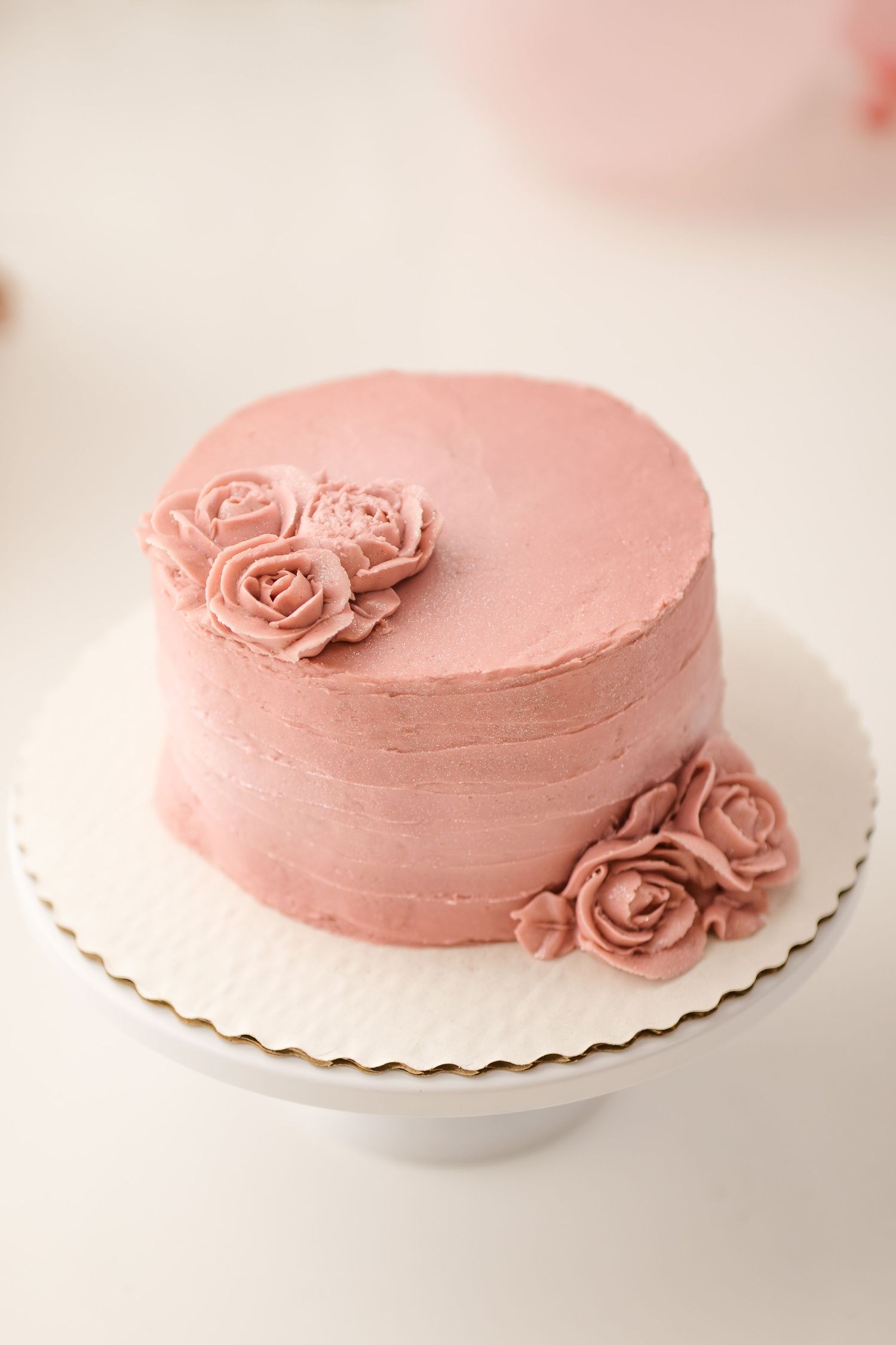 Elegant pink buttercream cake with rosette decorations on a white cake stand.
