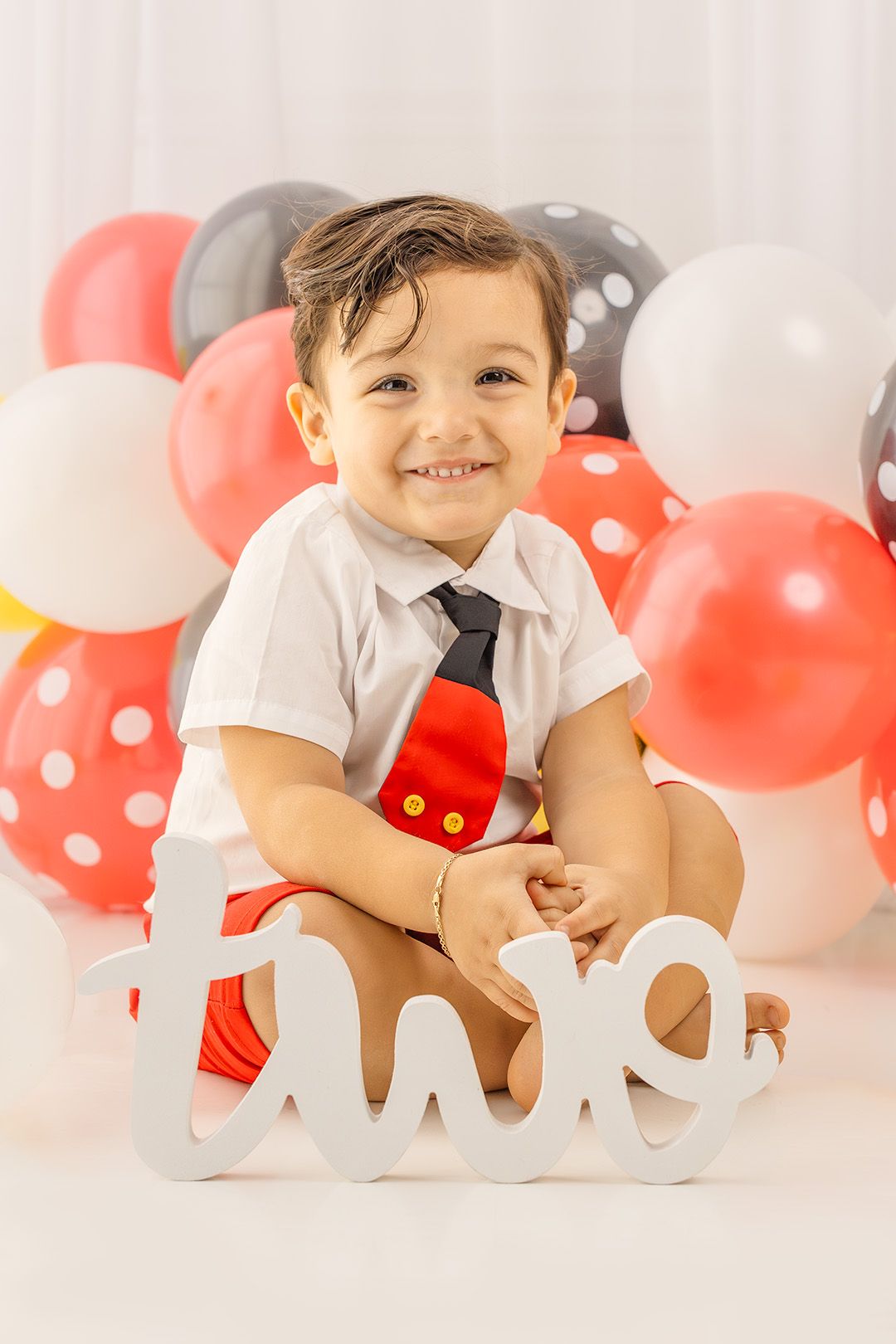 Happy toddler boy sitting in front of colorful balloons with a wooden 