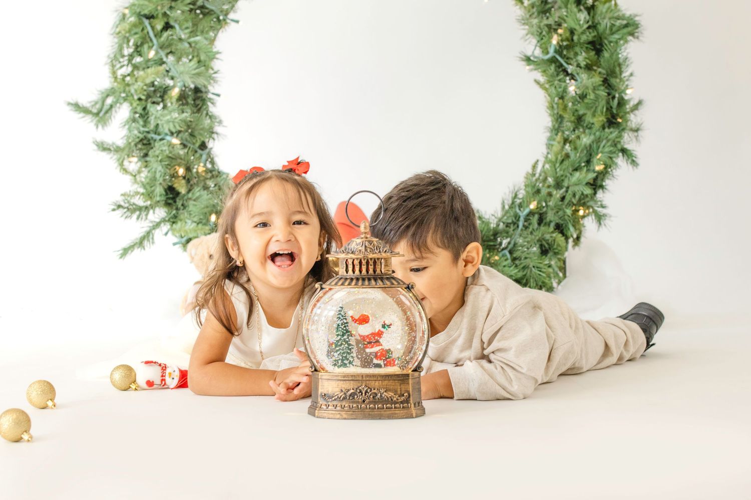 Children playing and laughing with holiday decorations and greenery in a bright white studio setting.