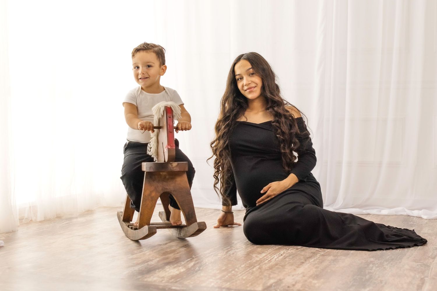 Family portrait session in a bright white studio with a wooden rocking horse toy.