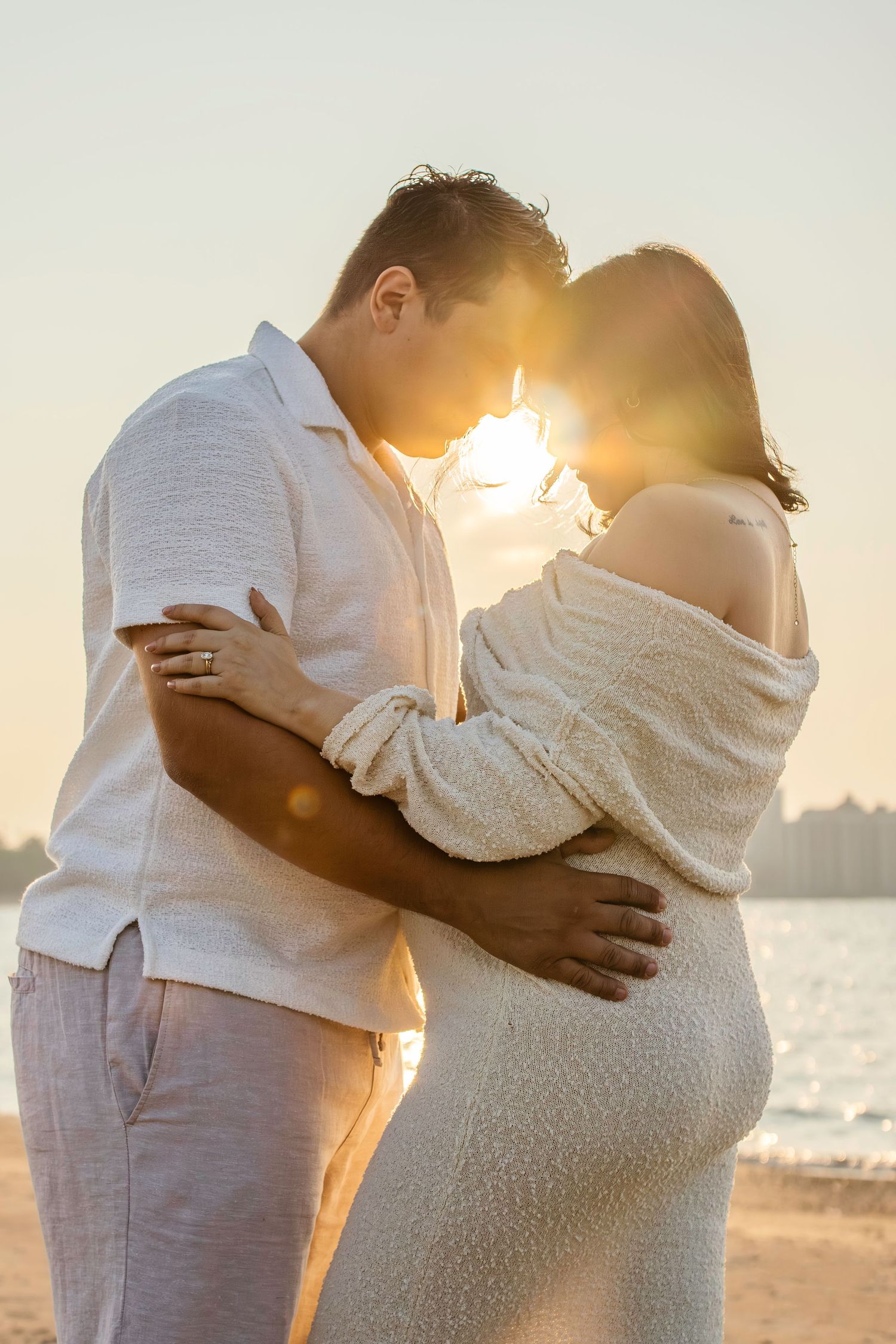 A romantic silhouette of a couple embracing on the beach at sunset, with the woman wearing a flowing white dress.
