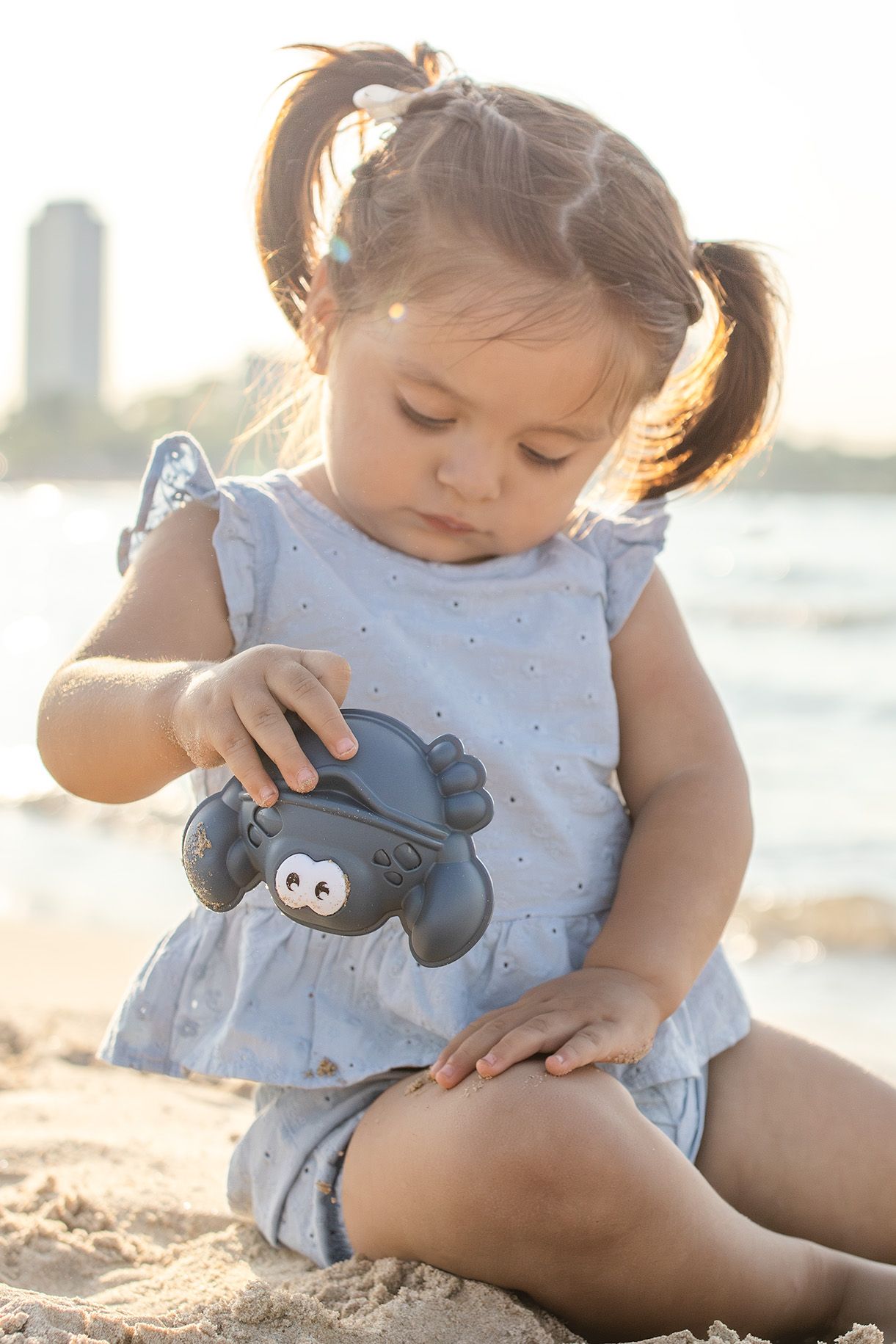 Toddler girl with pigtails playing with a toy crab on a sunny beach.