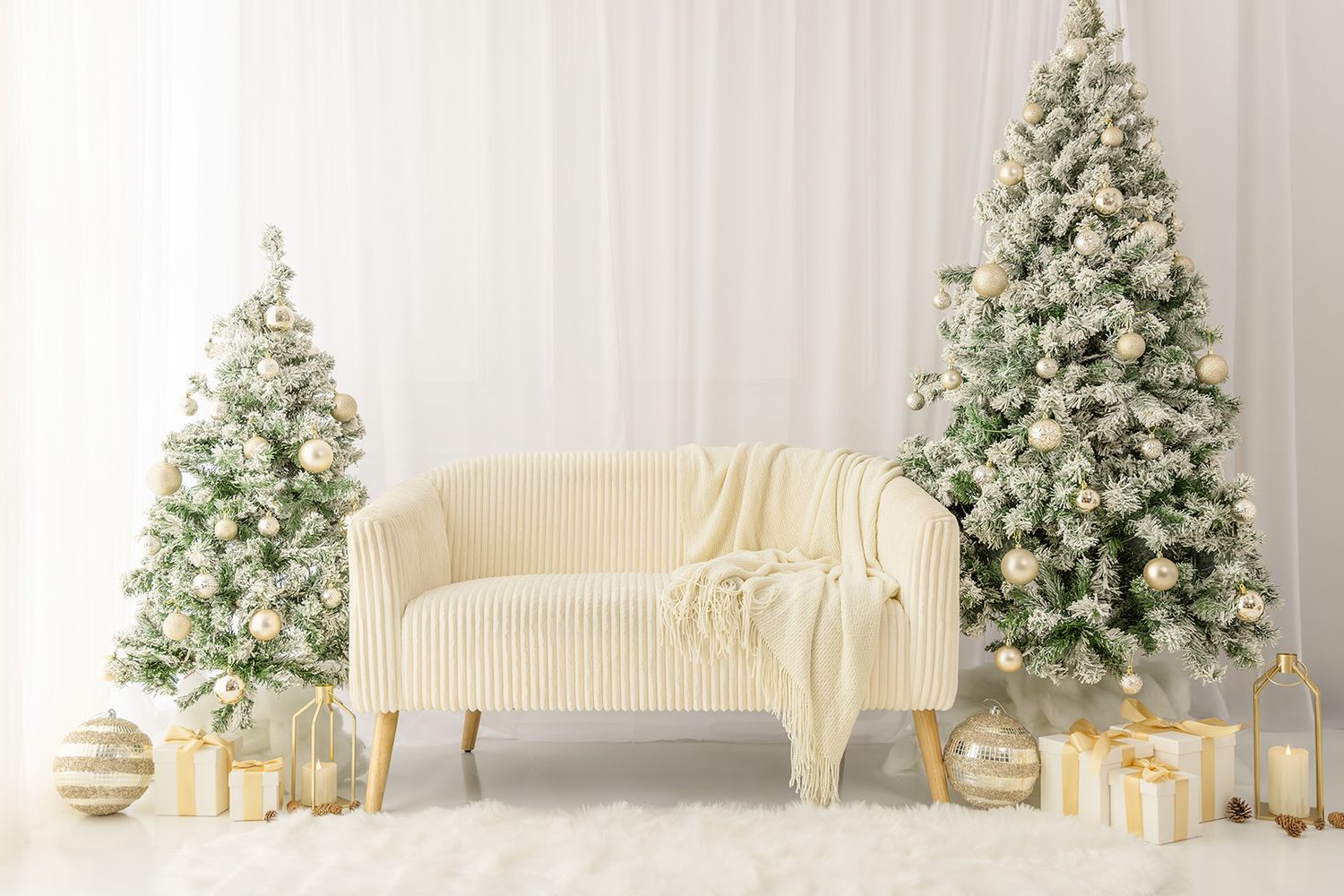 Elegant white Christmas setup with snowy trees, cream sofa, gold ornaments, and wrapped gifts on a fluffy rug.