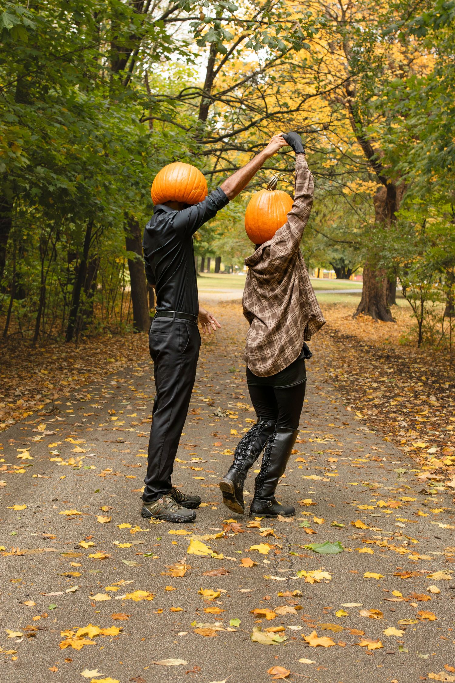 Two figures with pumpkin heads playfully interact in a fall scene with colorful leaves scattered on the ground.