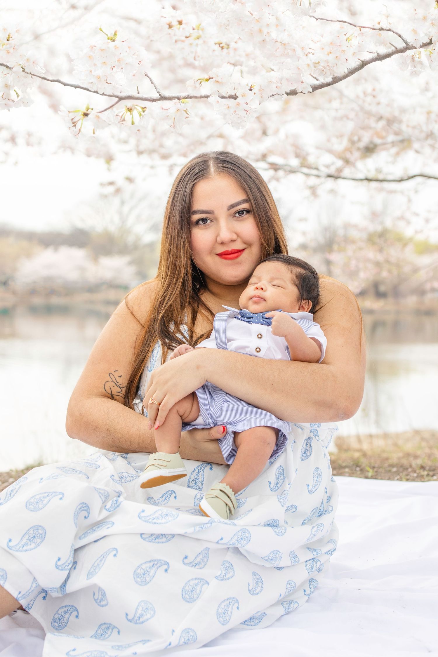 Beautiful spring portrait with a baby in light blue outfit sitting on a white blanket under blooming cherry blossoms.