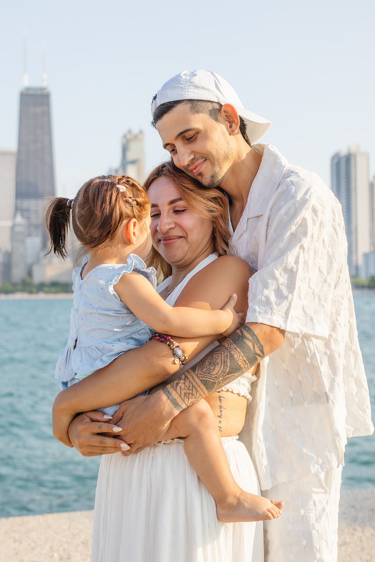 Happy family of three sharing a tender embrace by the Chicago lakefront on a sunny day.