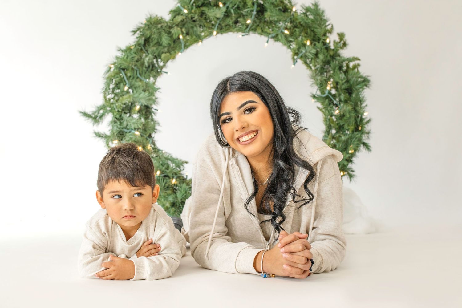 Two people lying on white floor with green foliage decorations above them creating a cozy holiday scene.