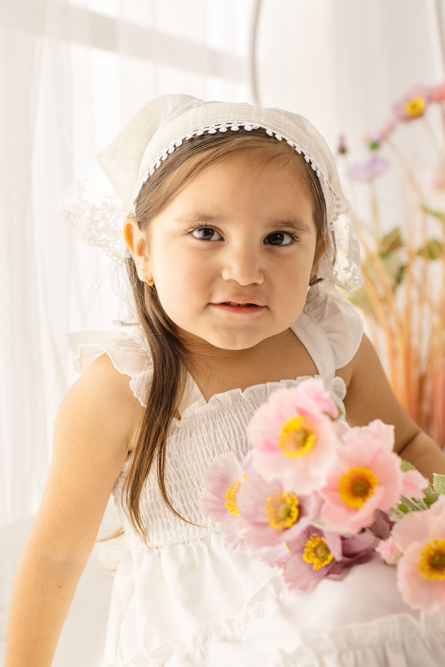 Young girl in white dress and bonnet holding pink flowers, portrait photo.
