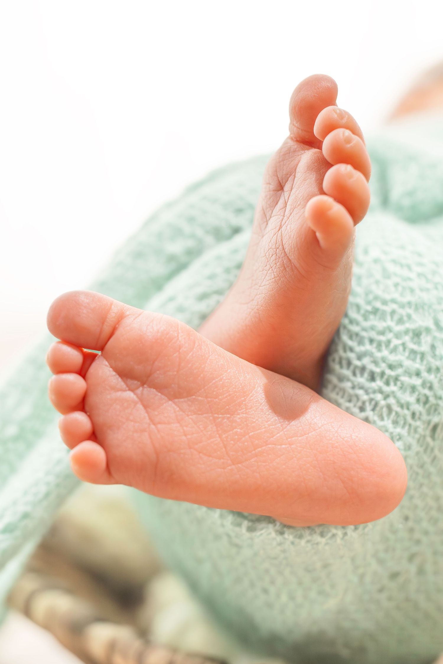 Close-up photo of tiny newborn baby feet resting on mint green knitted blanket.