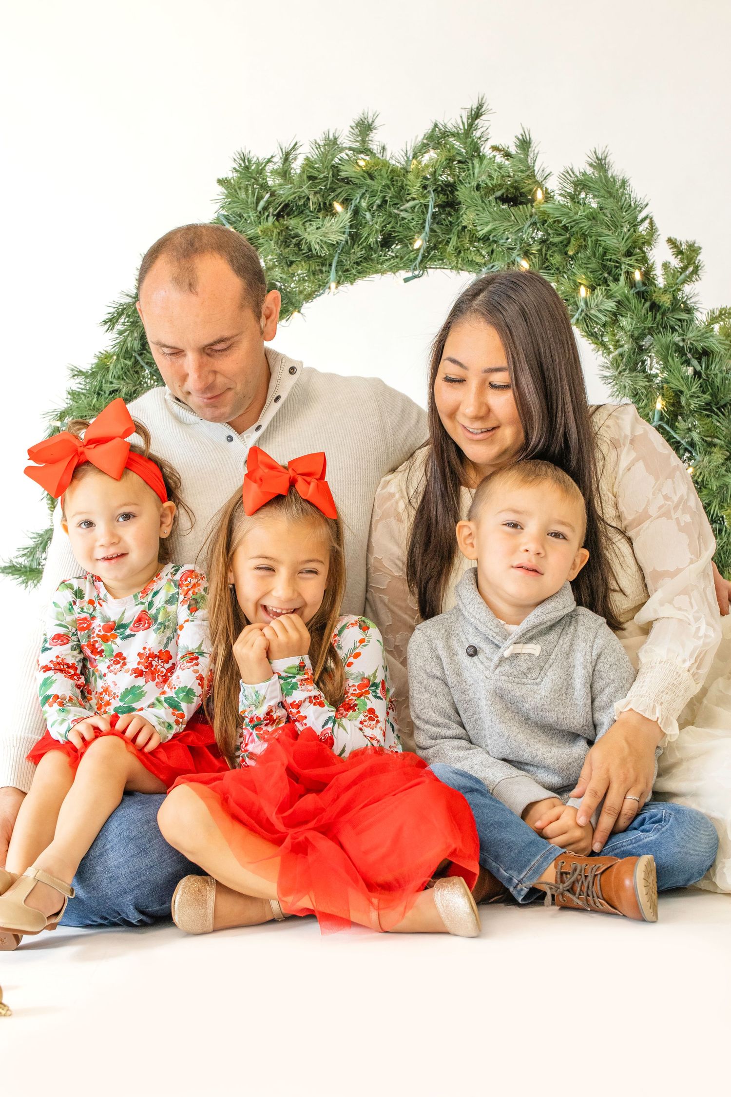 A festive holiday portrait of a family in coordinated outfits lounging together with greenery and red accents.