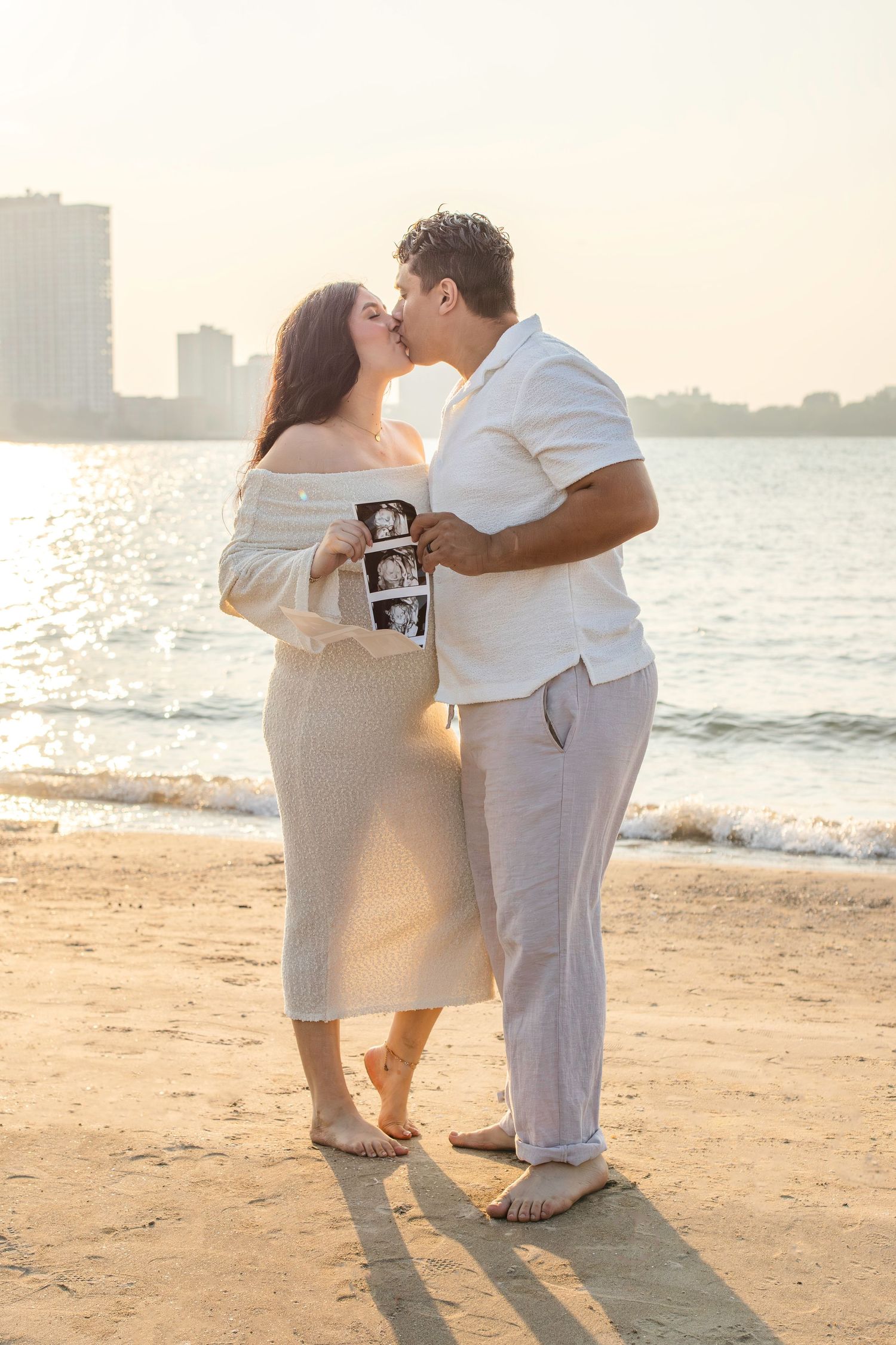Romantic sunset beach photography of a couple embracing with cityscape in background during golden hour.