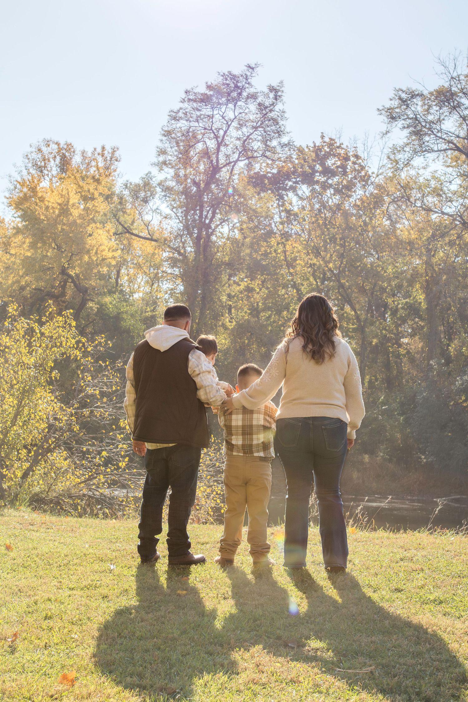A group of people stand together on a grassy hillside during golden hour with sunlight streaming behind them.