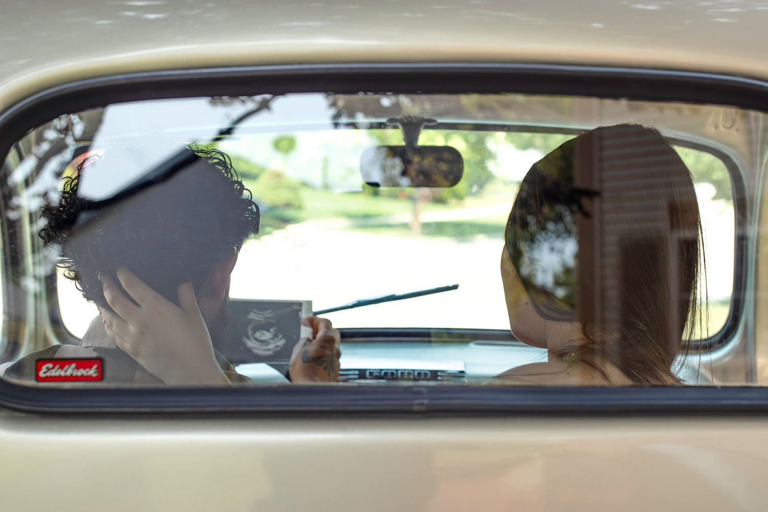 View through a car's rear window of two people sitting in front seats of a classic vehicle.