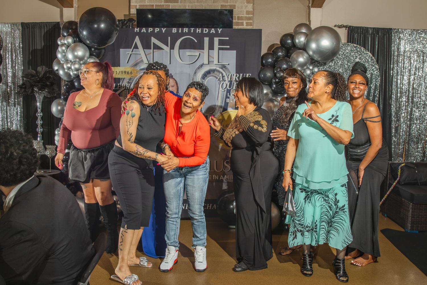 Group of women celebrating Angie's birthday party with balloons and decorations at an indoor venue.