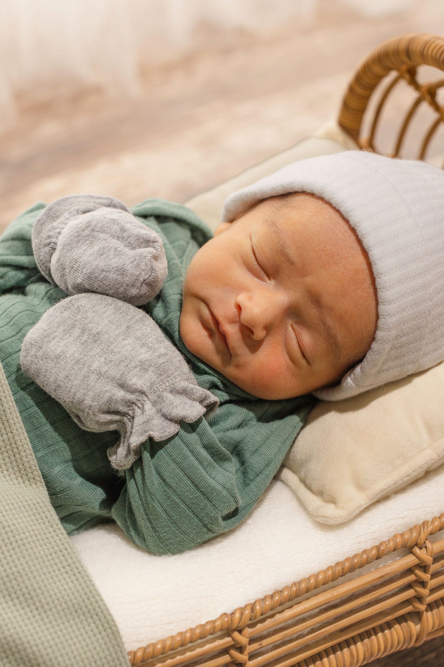 Newborn baby sleeping peacefully in a mint green outfit with gray accents on a woven bassinet.