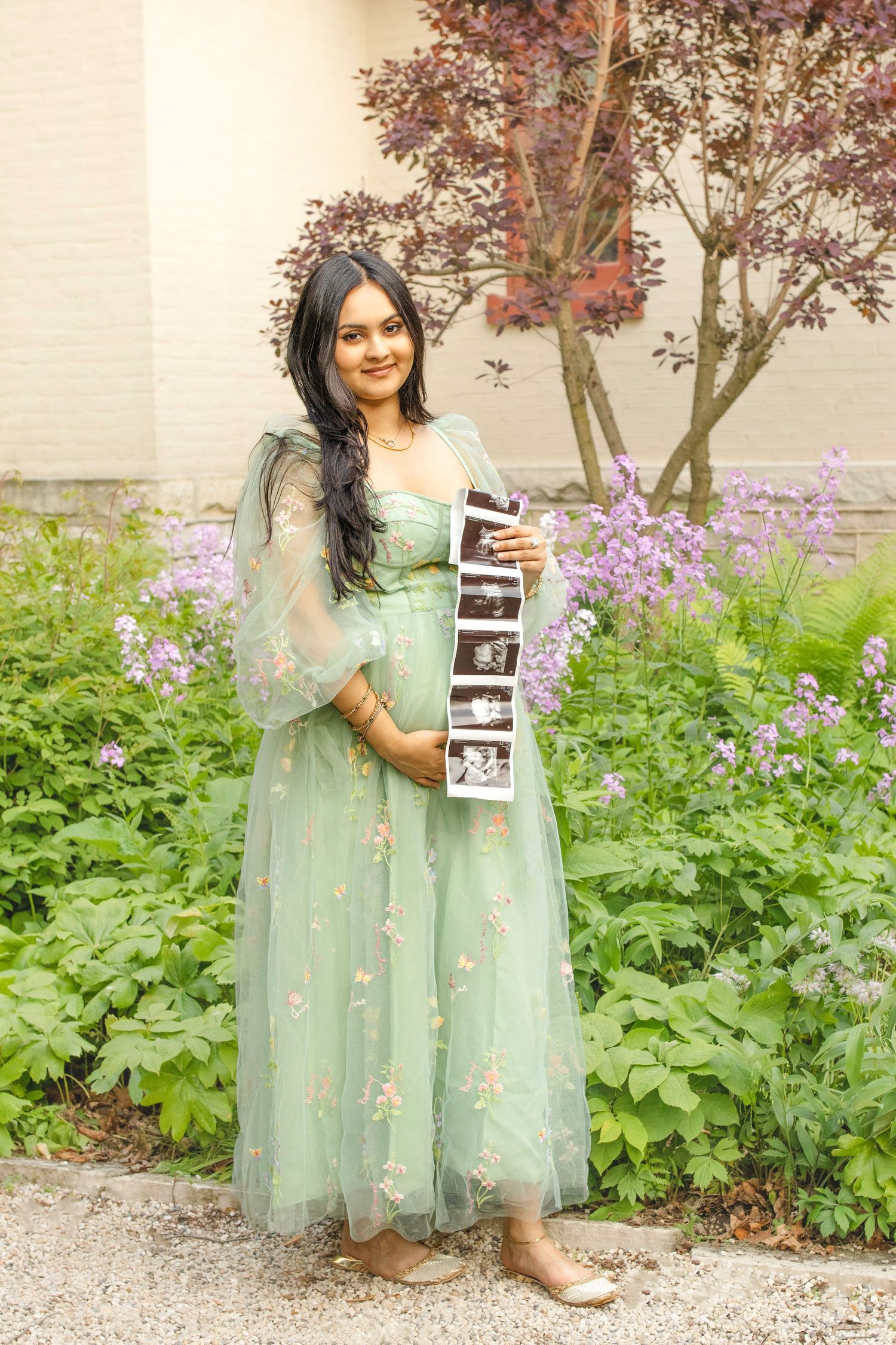 Beautiful sage green tulle dress with delicate floral embroidery shown in a garden setting with purple blooms.