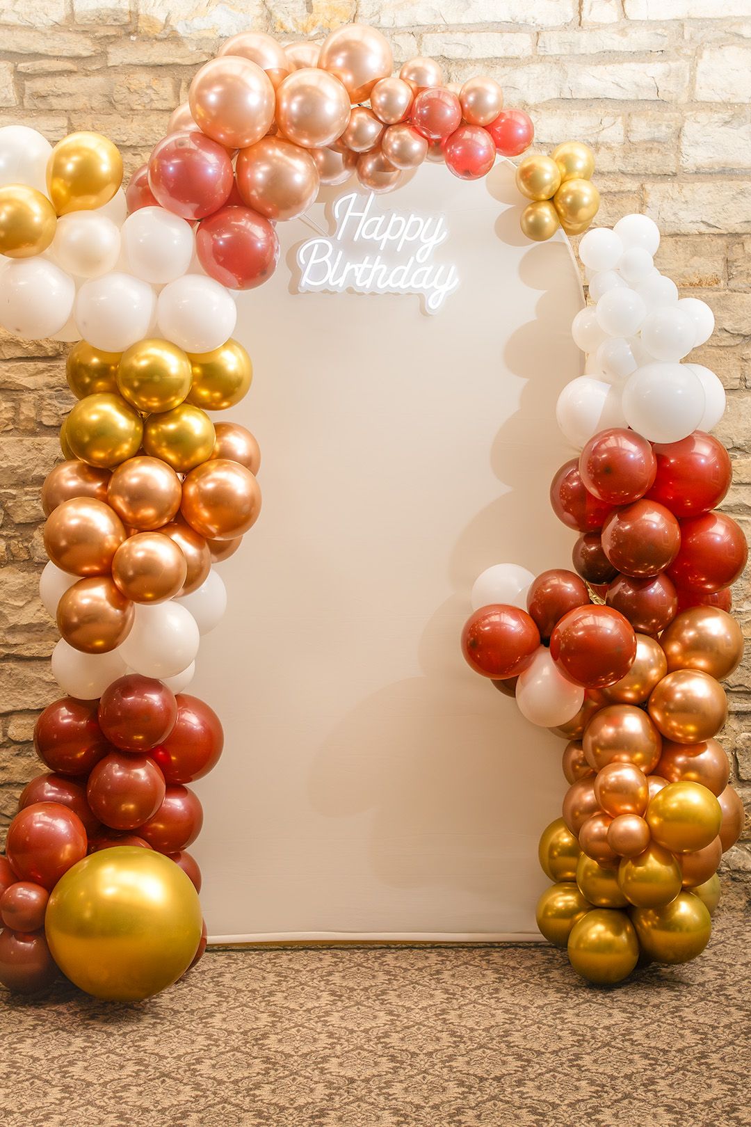 Elegant birthday photo backdrop with colorful balloon arch in gold, red, and white, featuring a neon Happy Birthday sign.