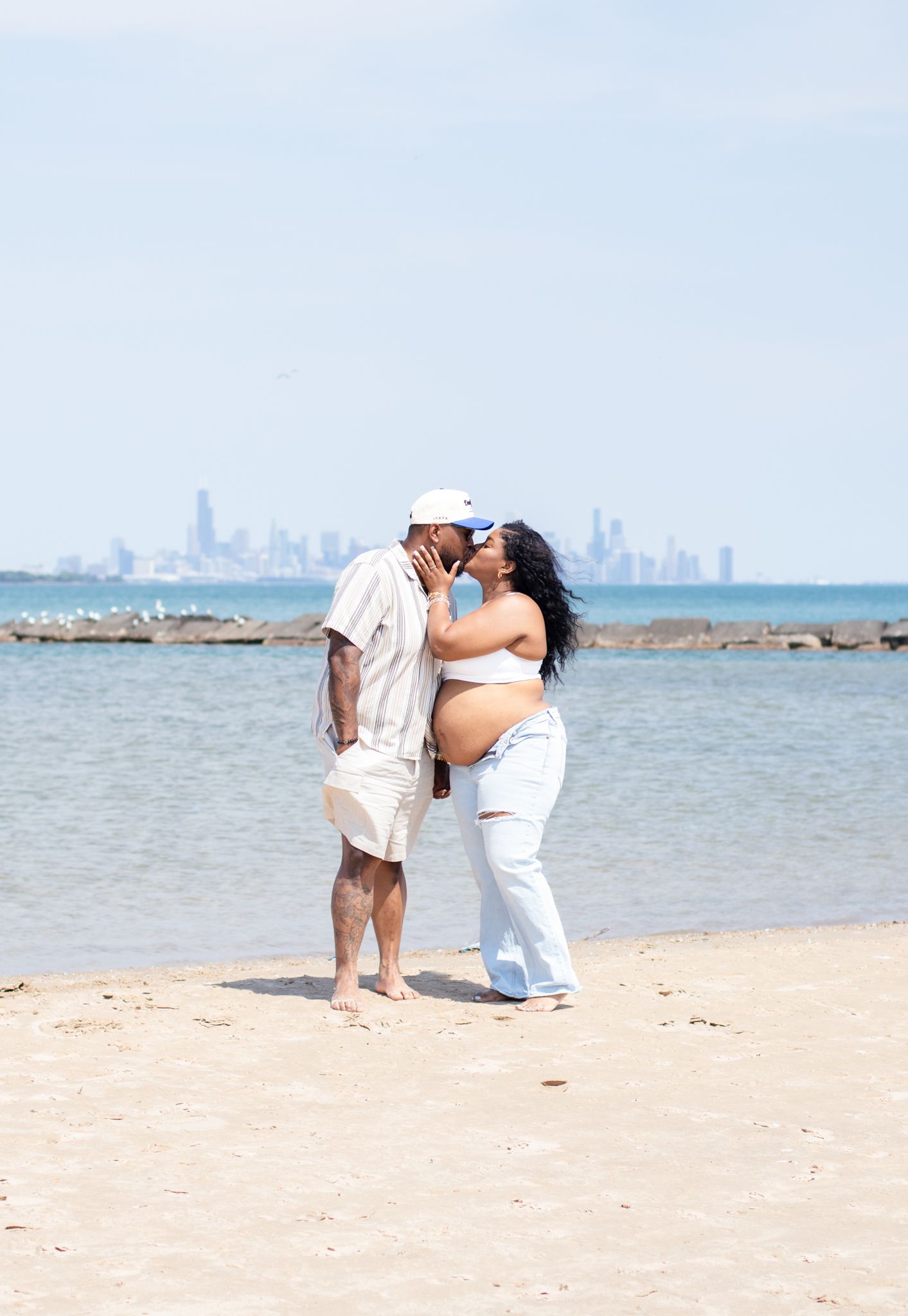Romantic beach portrait with city skyline visible across water in background.
