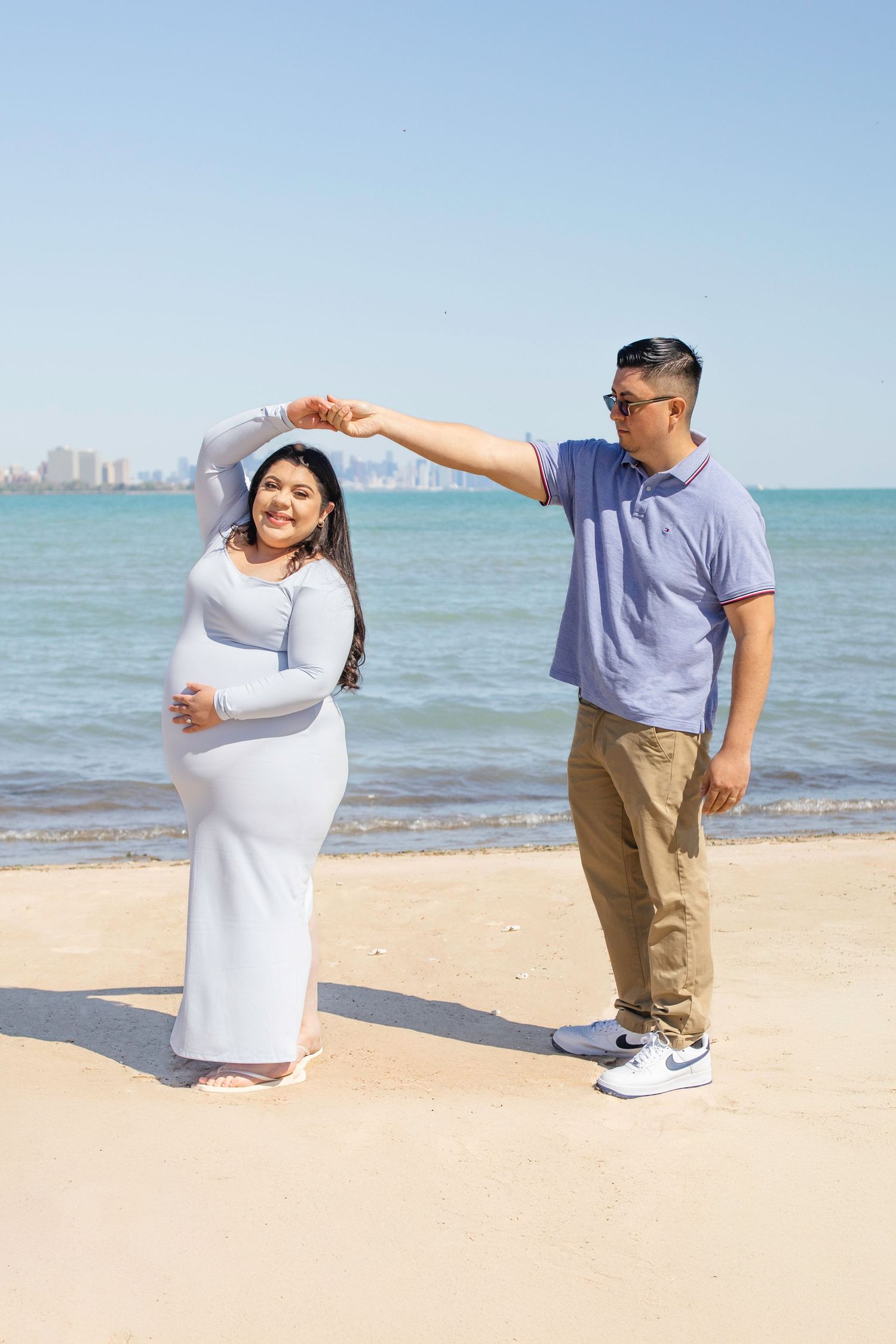A couple poses together on a beach while dancing, with the skyline of Chicago visible in the background over Lake Michigan.