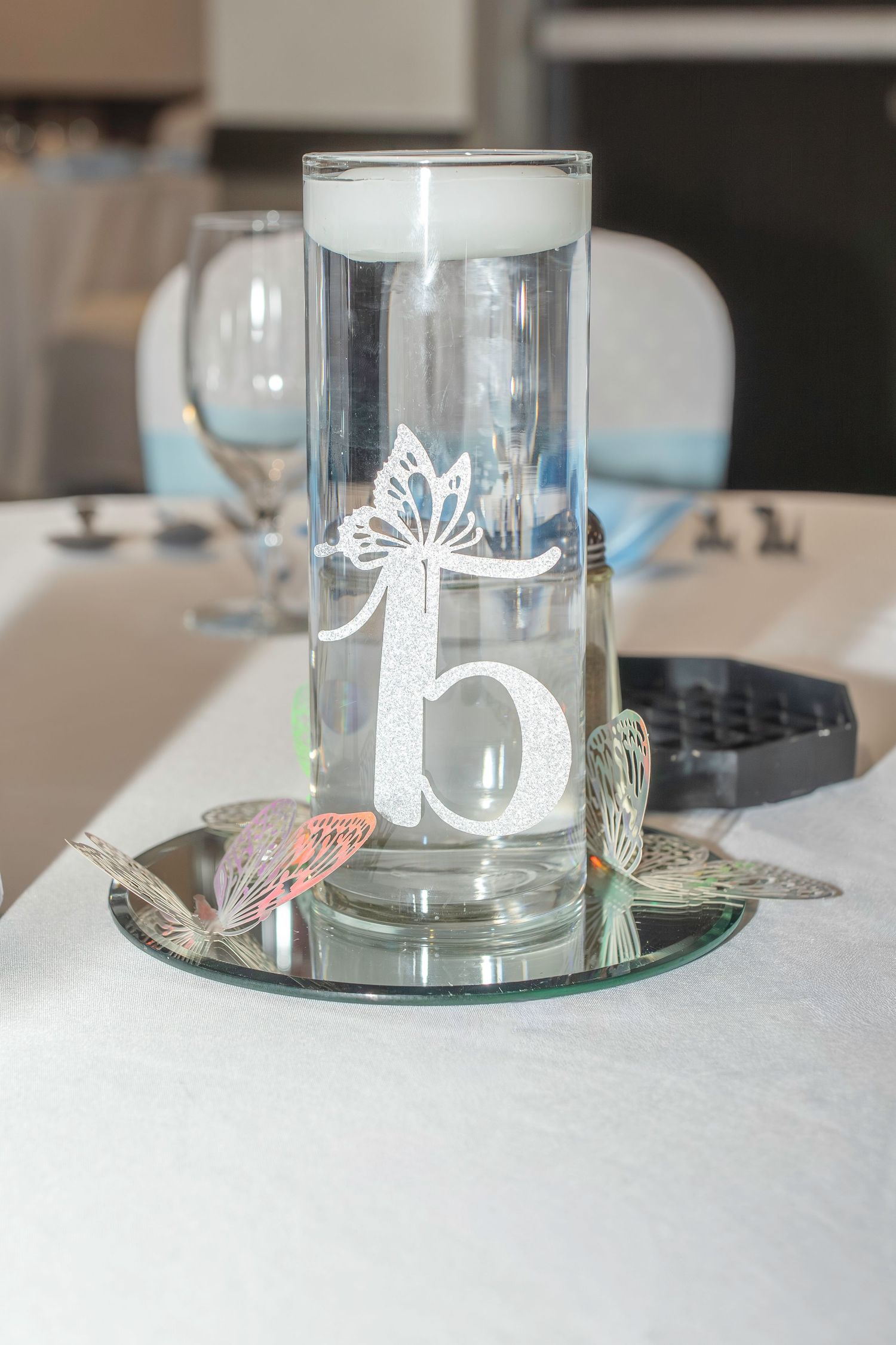 Decorative glass candle holders with intricate butterfly designs sit atop mirrored surfaces creating an elegant table setting.