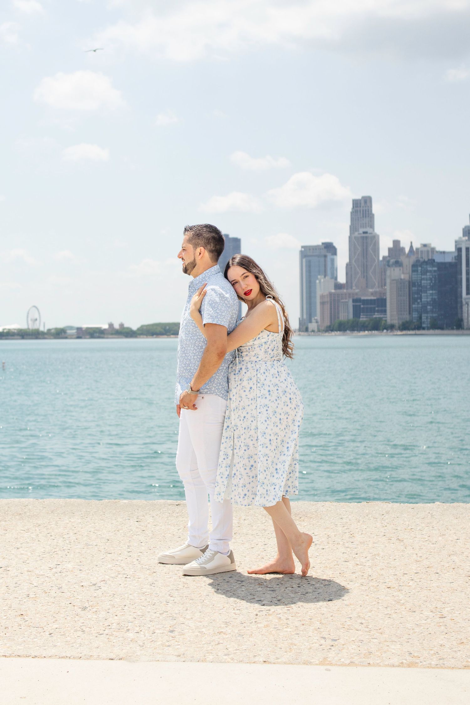 A couple shares a romantic moment on a beach with the Chicago skyline visible across Lake Michigan on a sunny day.