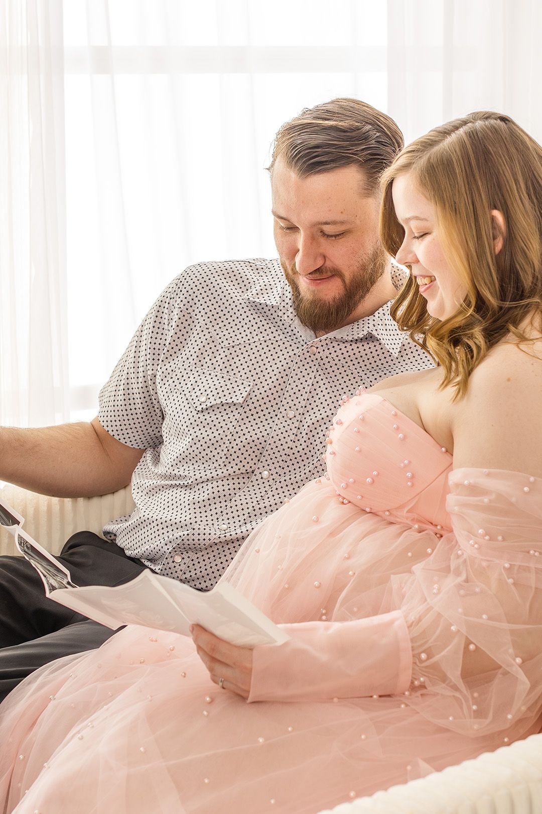 Couple in casual attire sharing an intimate moment while reading together on a white couch.