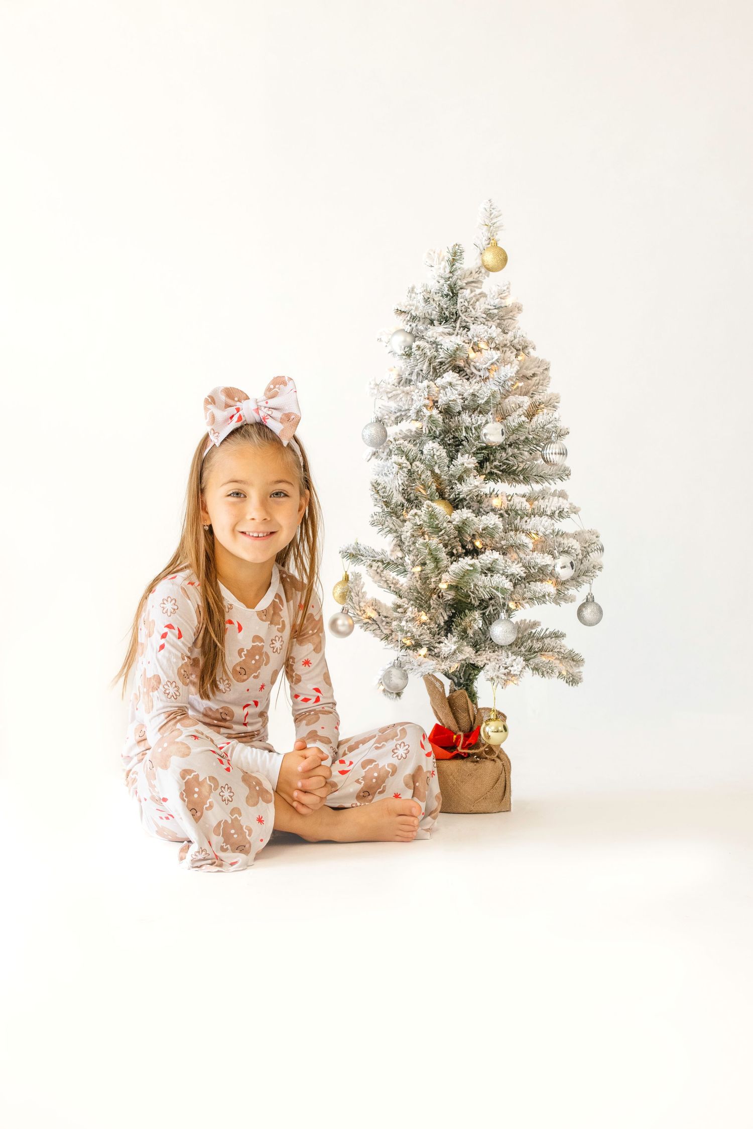 Children pose playfully on white backdrop with small flocked Christmas tree and holiday decorations.