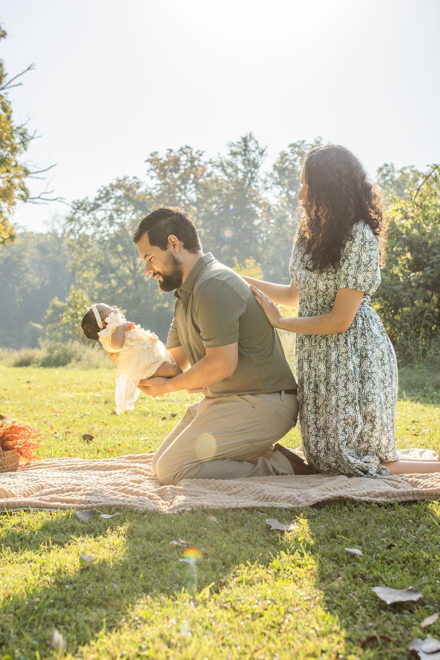 Family sits together on blanket in grassy field during golden hour photoshoot with newborn.