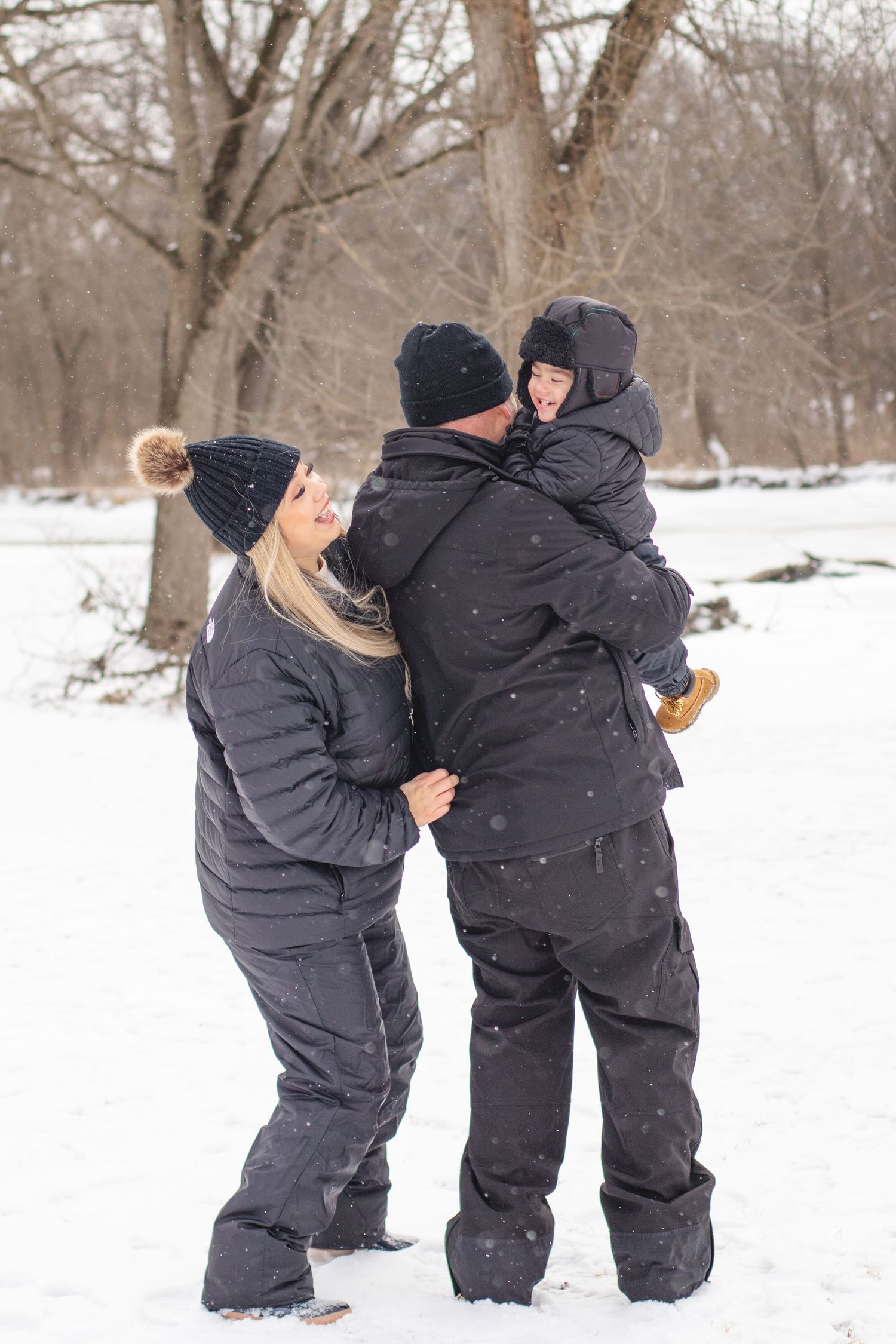 Family wearing winter coats embraces together in a snowy winter forest setting.