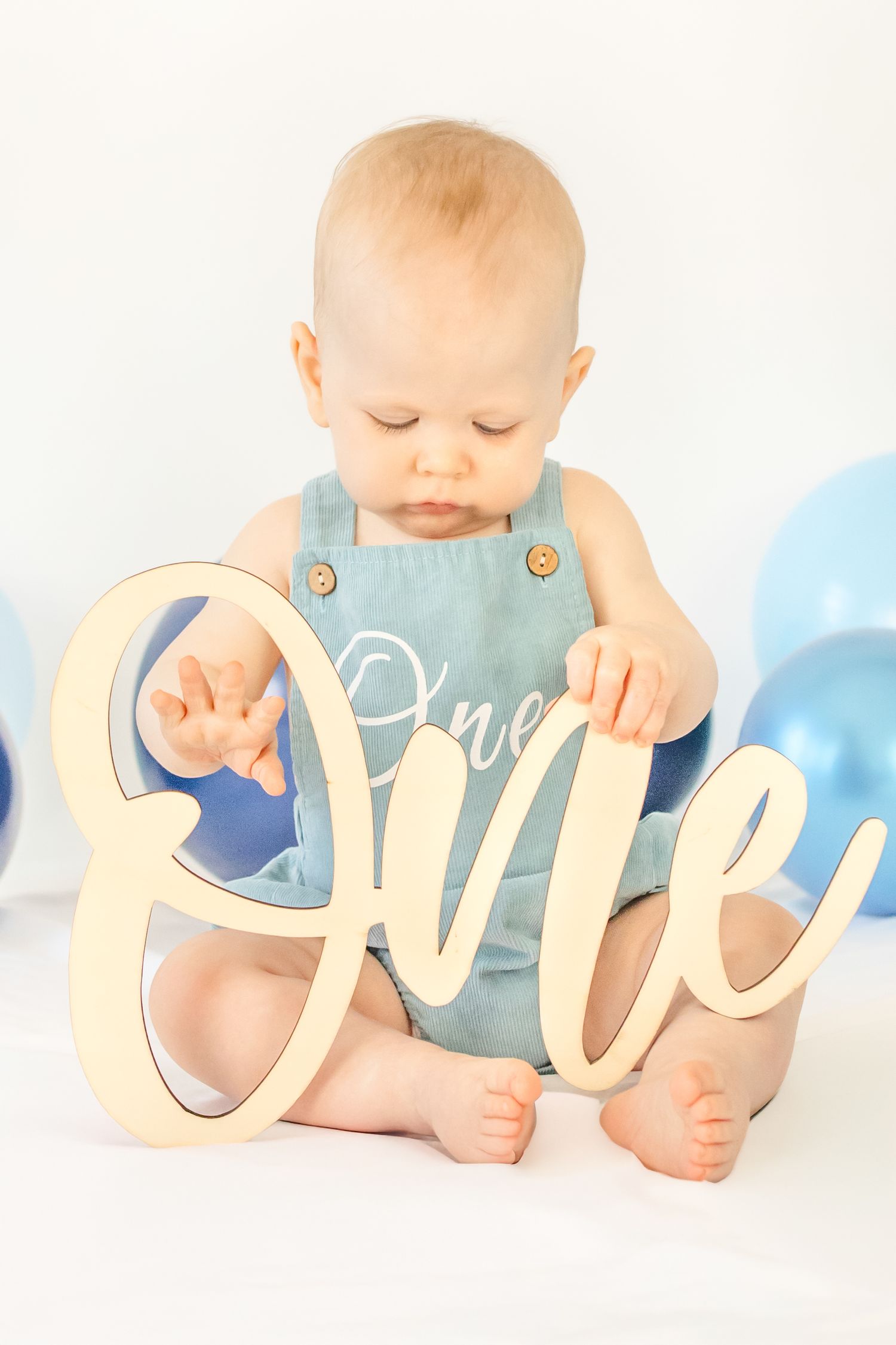 Baby in blue romper holding wooden 
