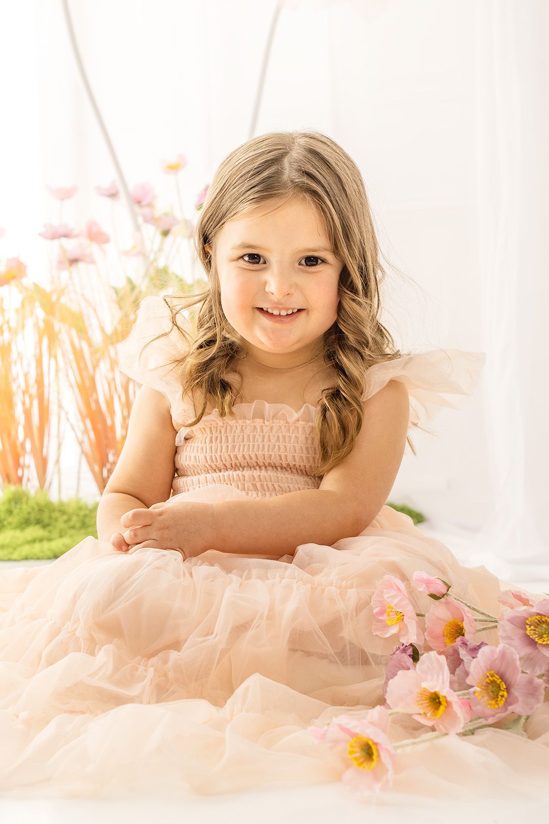 A series of three soft pink portraits featuring a child in a peach tulle dress laying among delicate pink flowers.