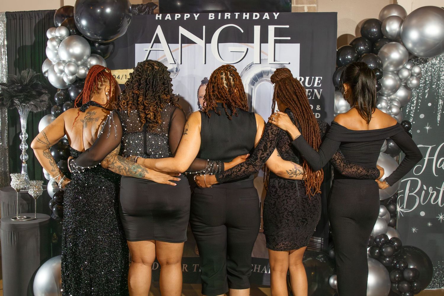 Group of women in black outfits posing together at Angie's birthday party with balloon decorations.