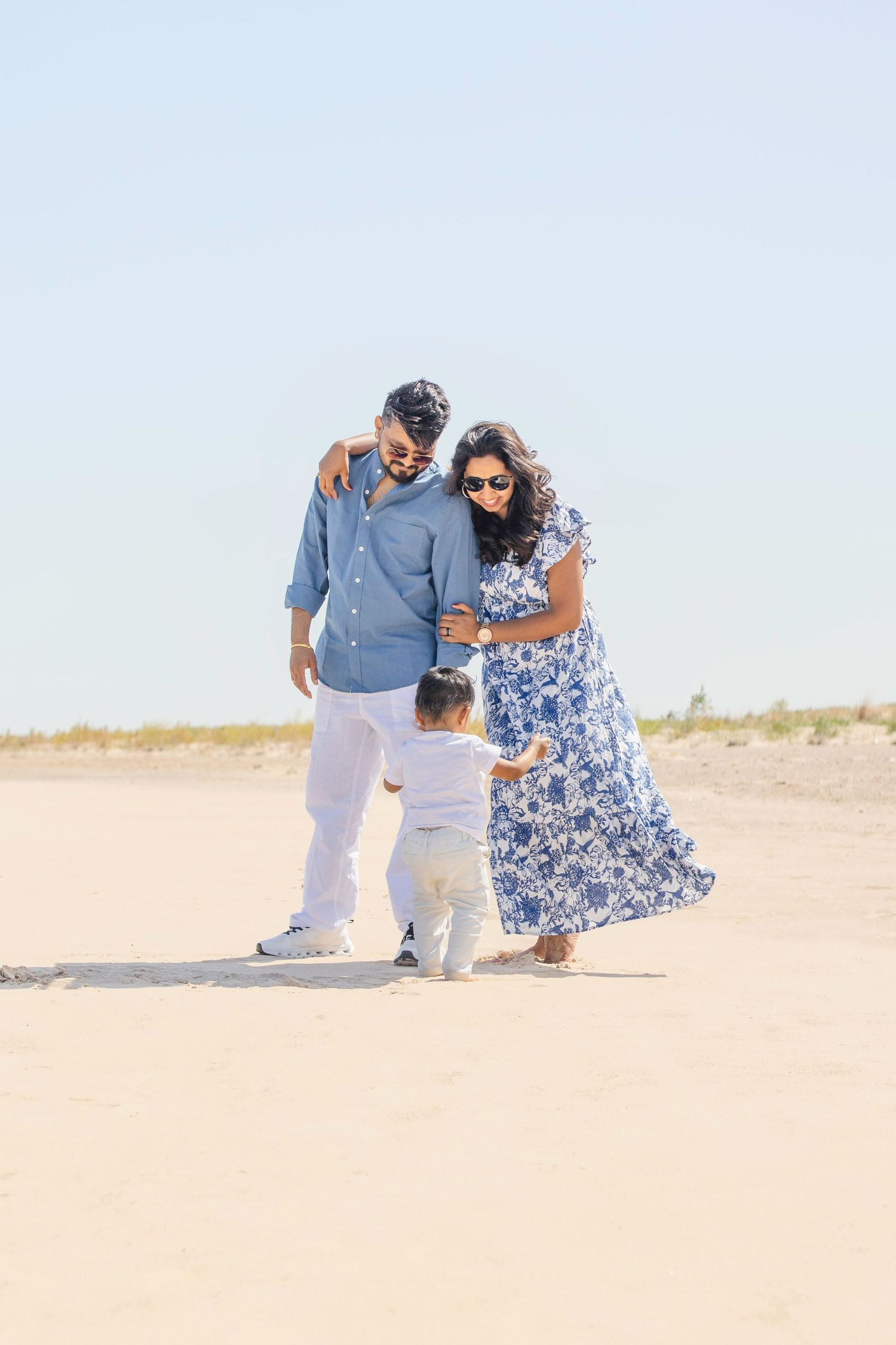 A family in coordinated blue and white outfits pose together on a sandy desert landscape.