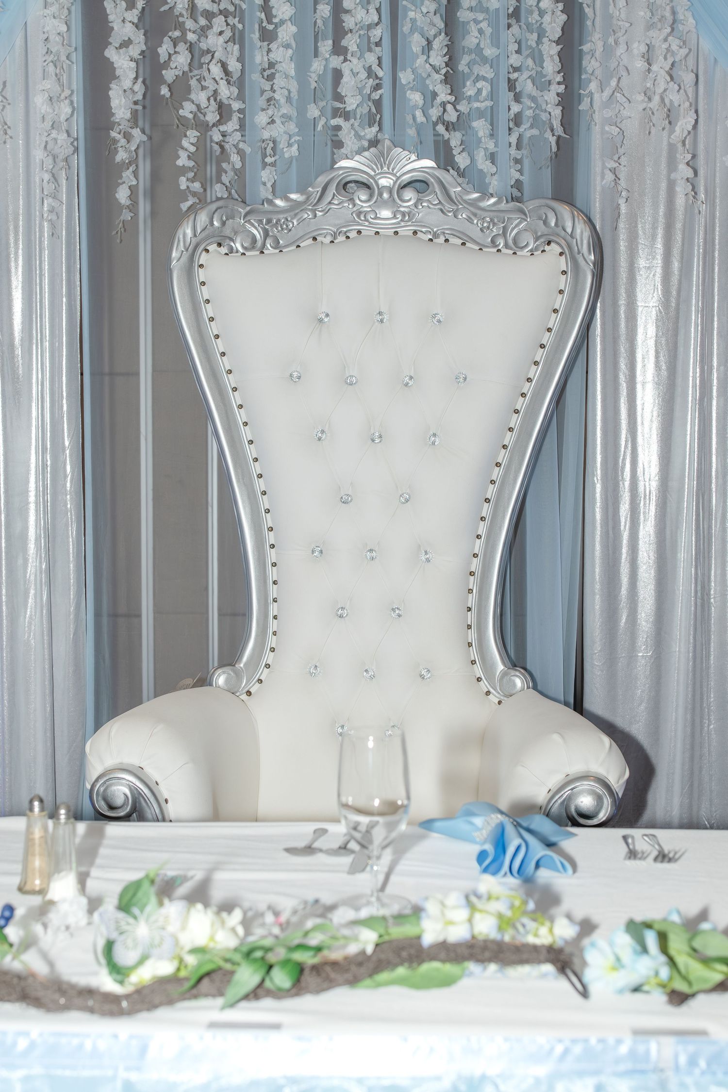 Luxury white ornate throne chairs with silver accents arranged in a row against a light curtain backdrop.