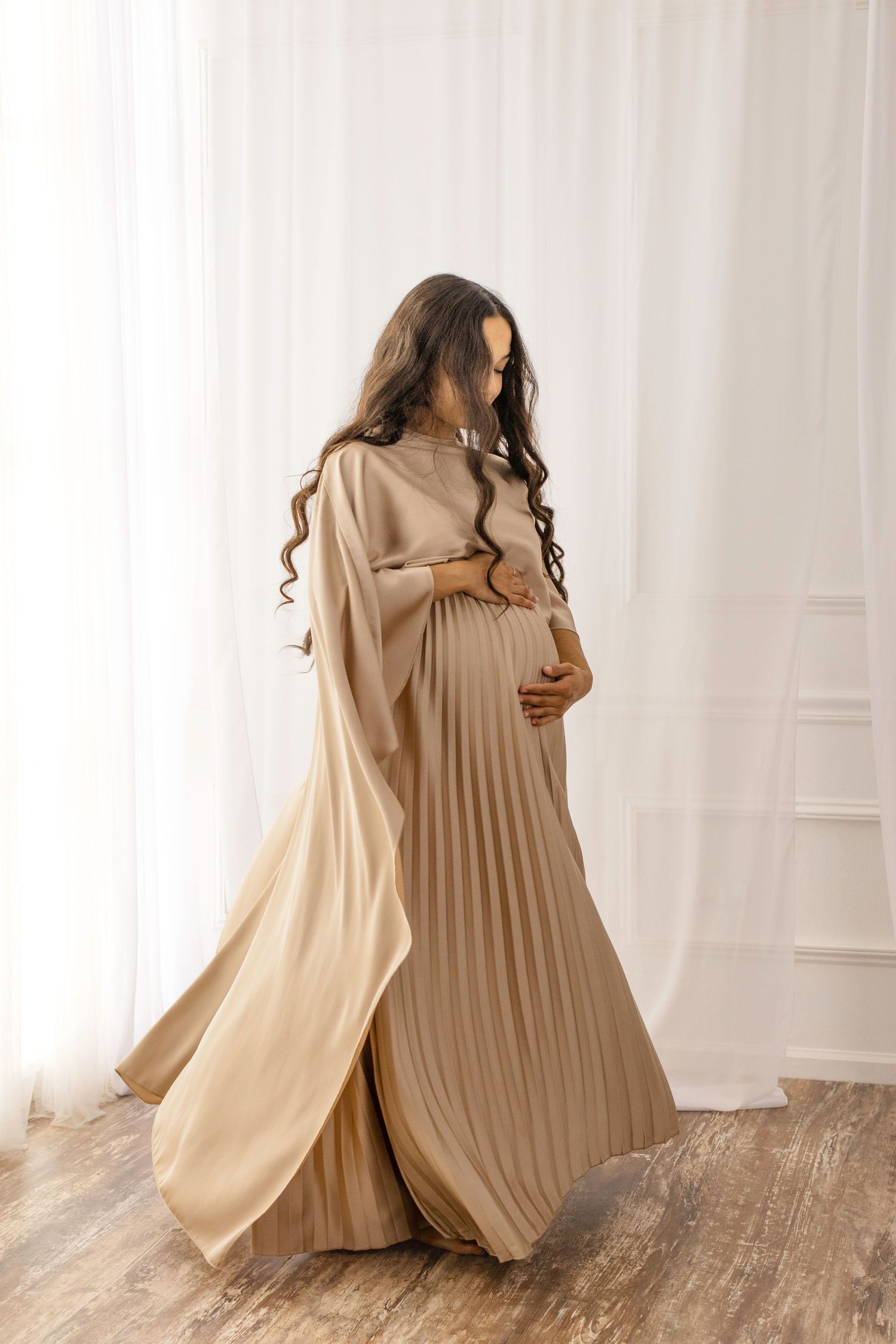 A series of four photos showing a person in a flowing beige dress and cape moving gracefully against a white backdrop.