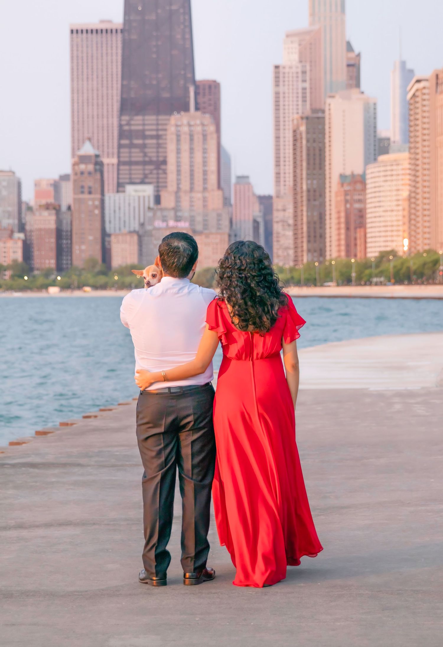 Two people in formal attire admire Chicago's skyline while standing on a pier along Lake Michigan at sunset.