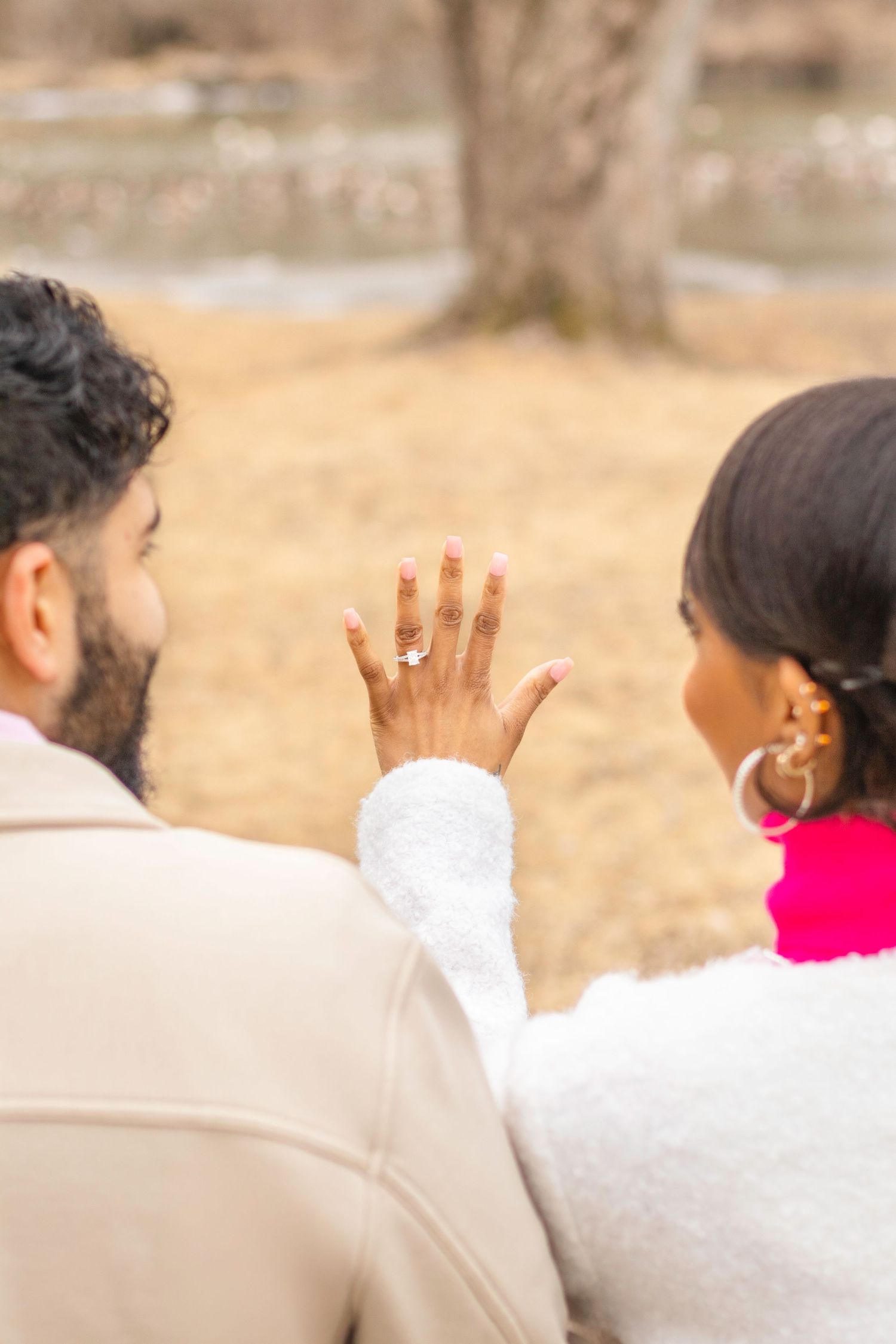Couple showing off engagement ring while sitting outdoors.