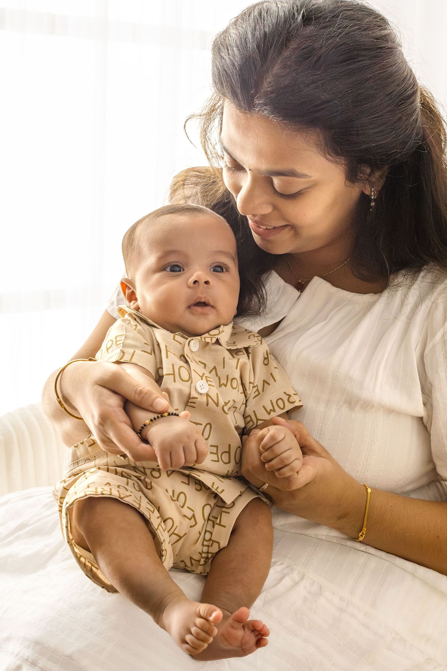 A tender moment captured between parent and baby wearing a beige ruffled outfit while lying on white bedding.