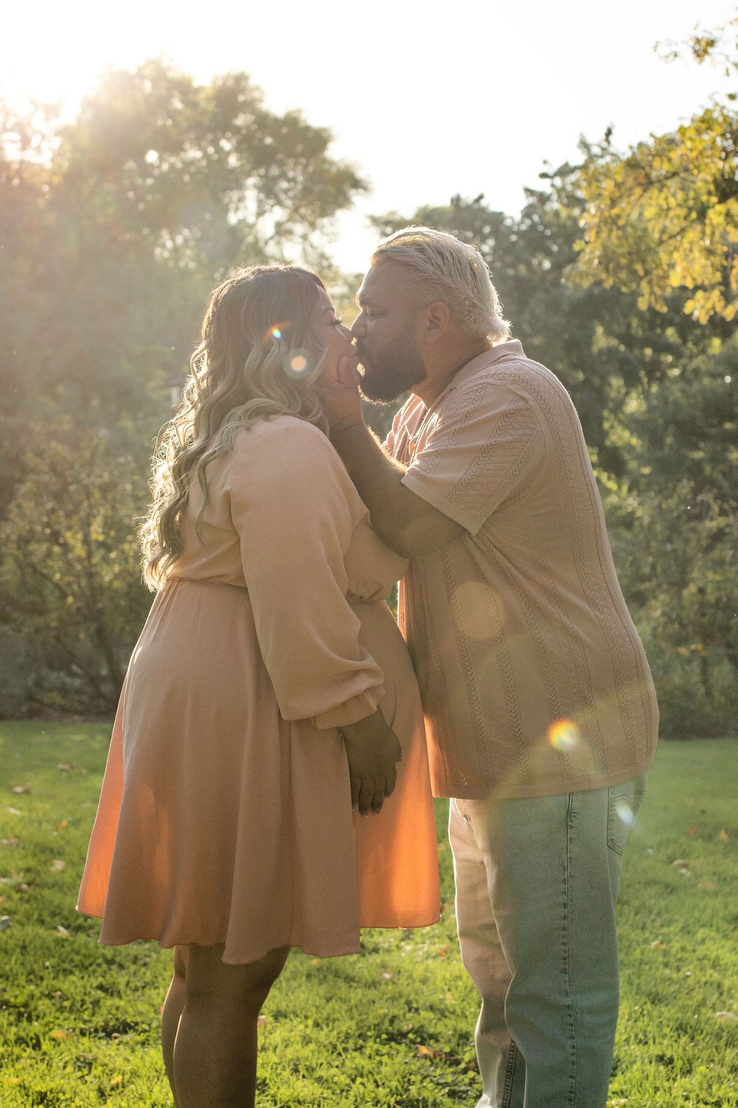 A romantic outdoor photo shoot in a sunlit park with warm golden light filtering through the trees.